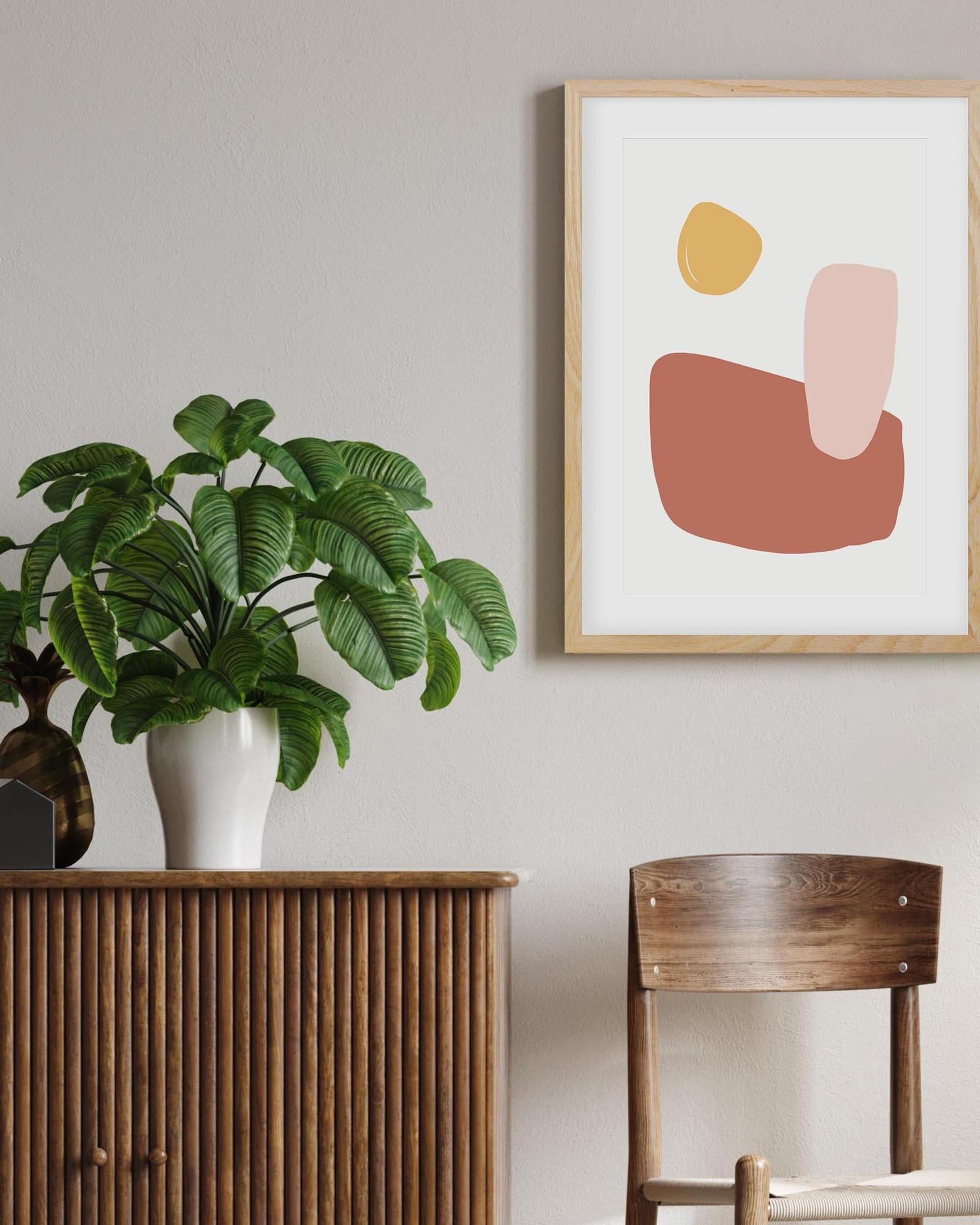 Abstract art print on a wall with a plant and wooden furniture in the foreground