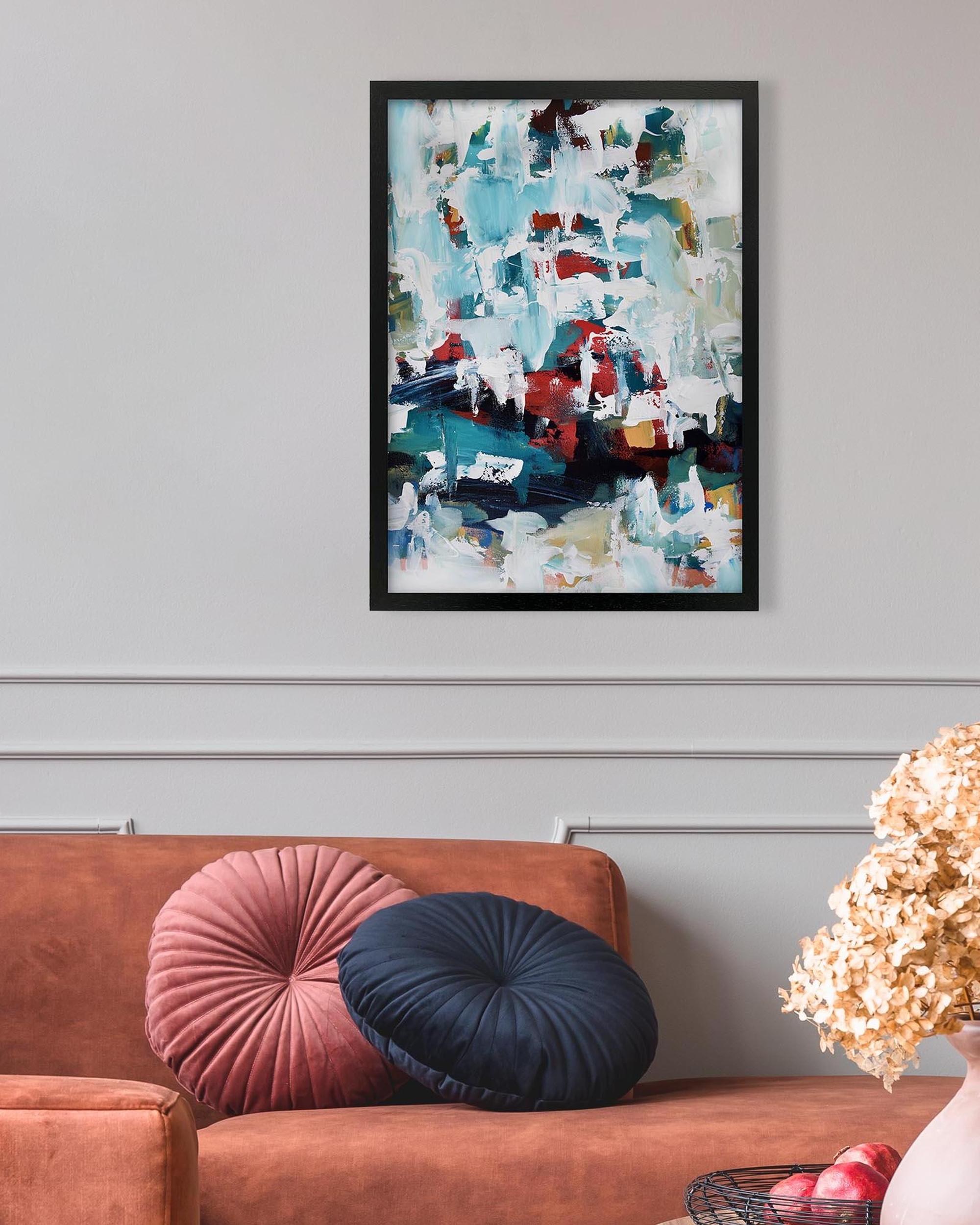 Abstract painting on a wall above a brown sofa with colorful cushions.