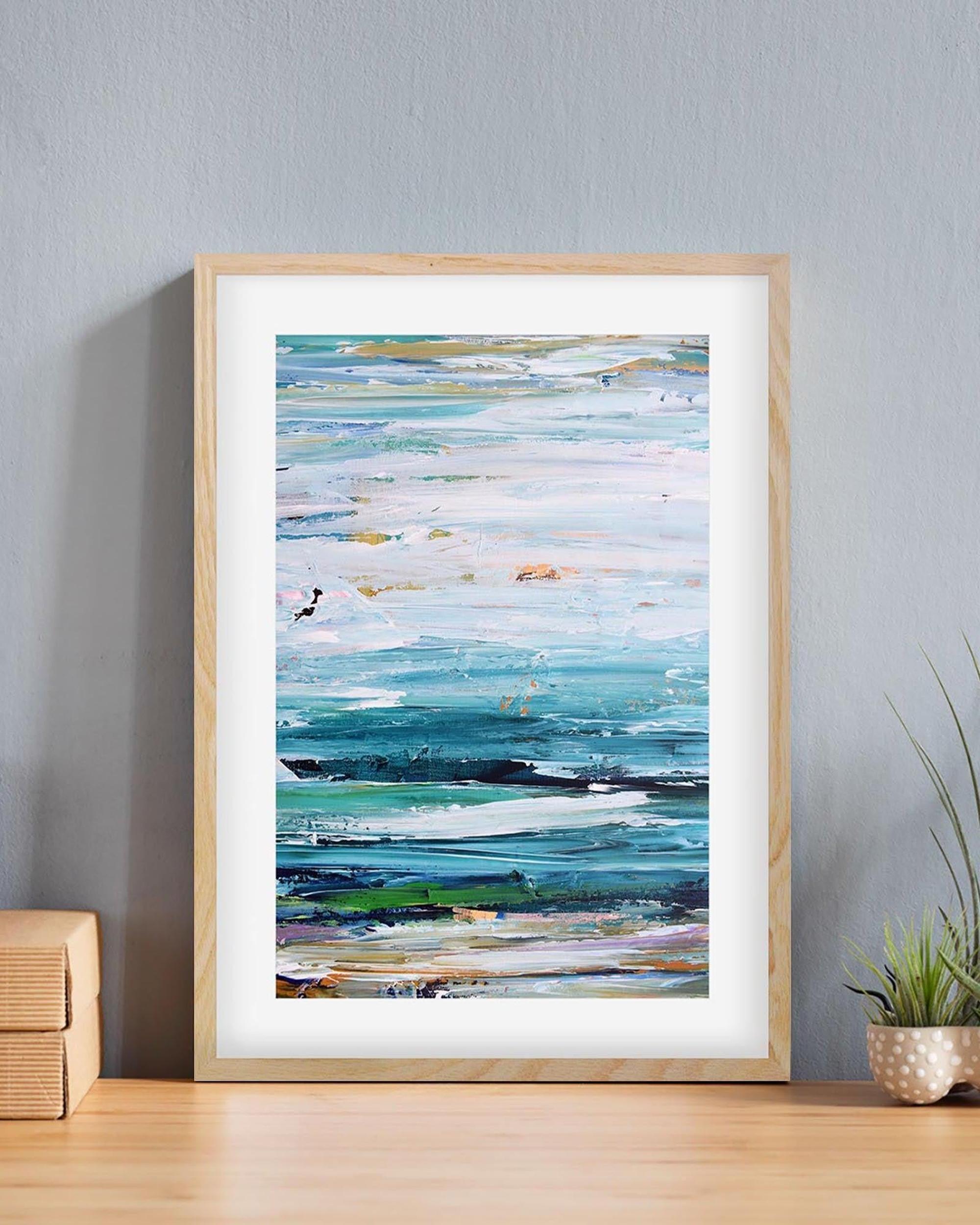 Framed abstract artwork on a wall with a plant and wooden box below.