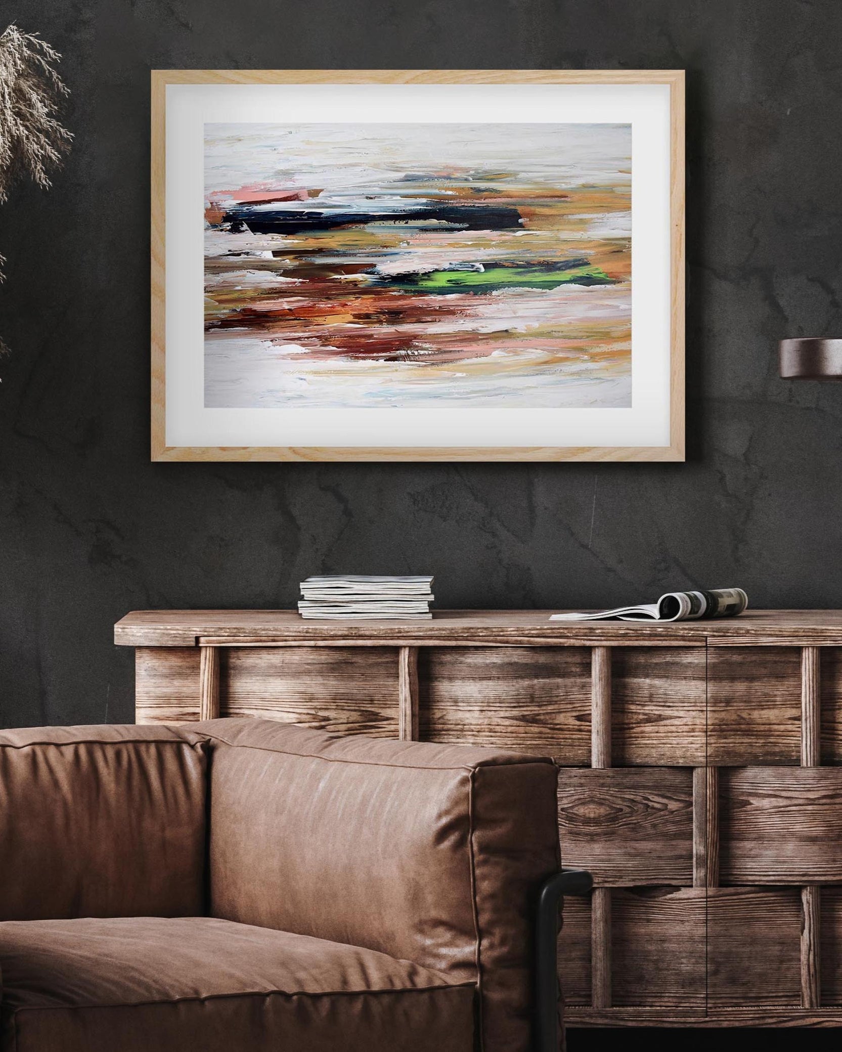 Framed abstract painting on a dark wall above a brown sofa and wooden cabinet.