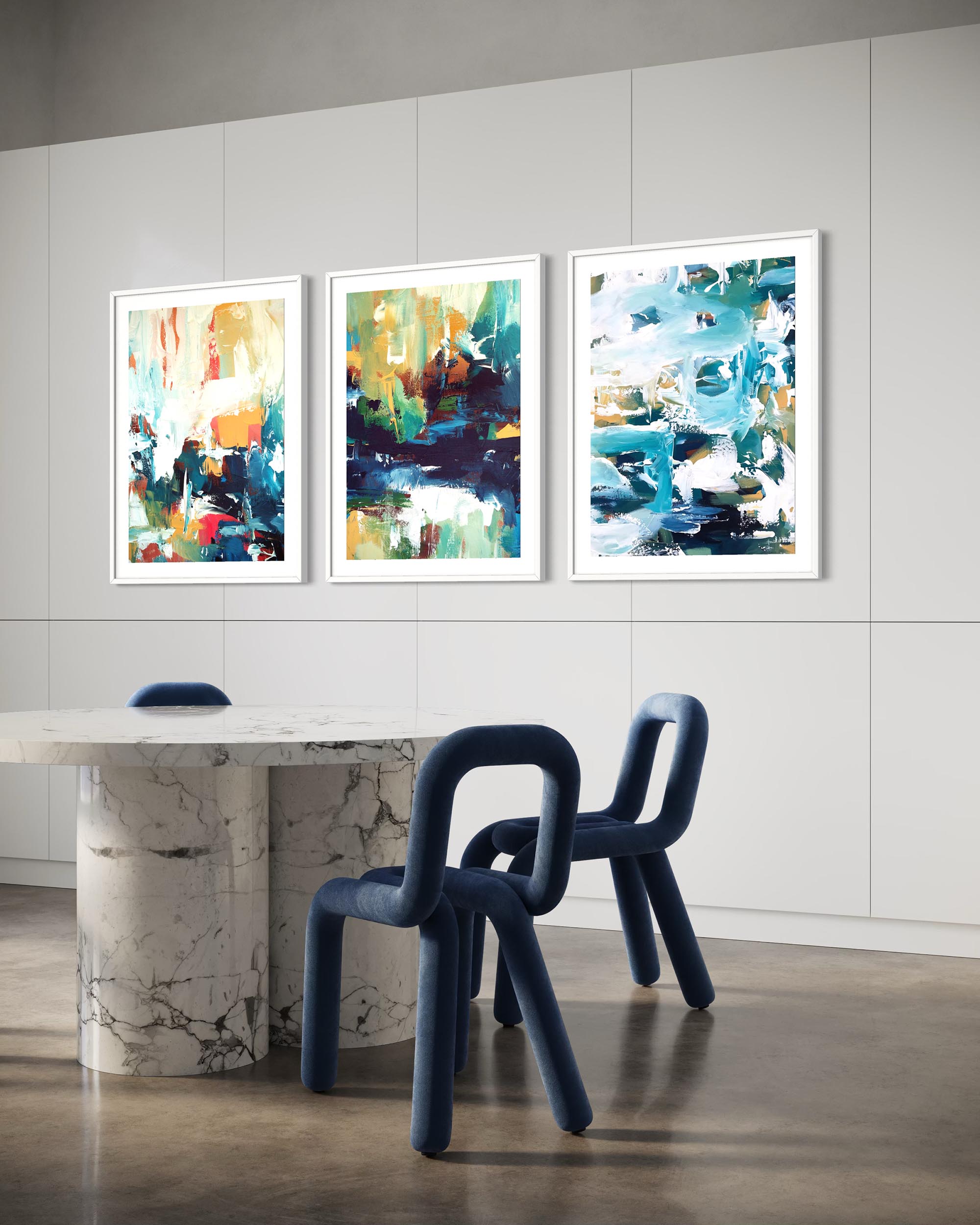 Three abstract paintings on a wall above a dining table with blue chairs.