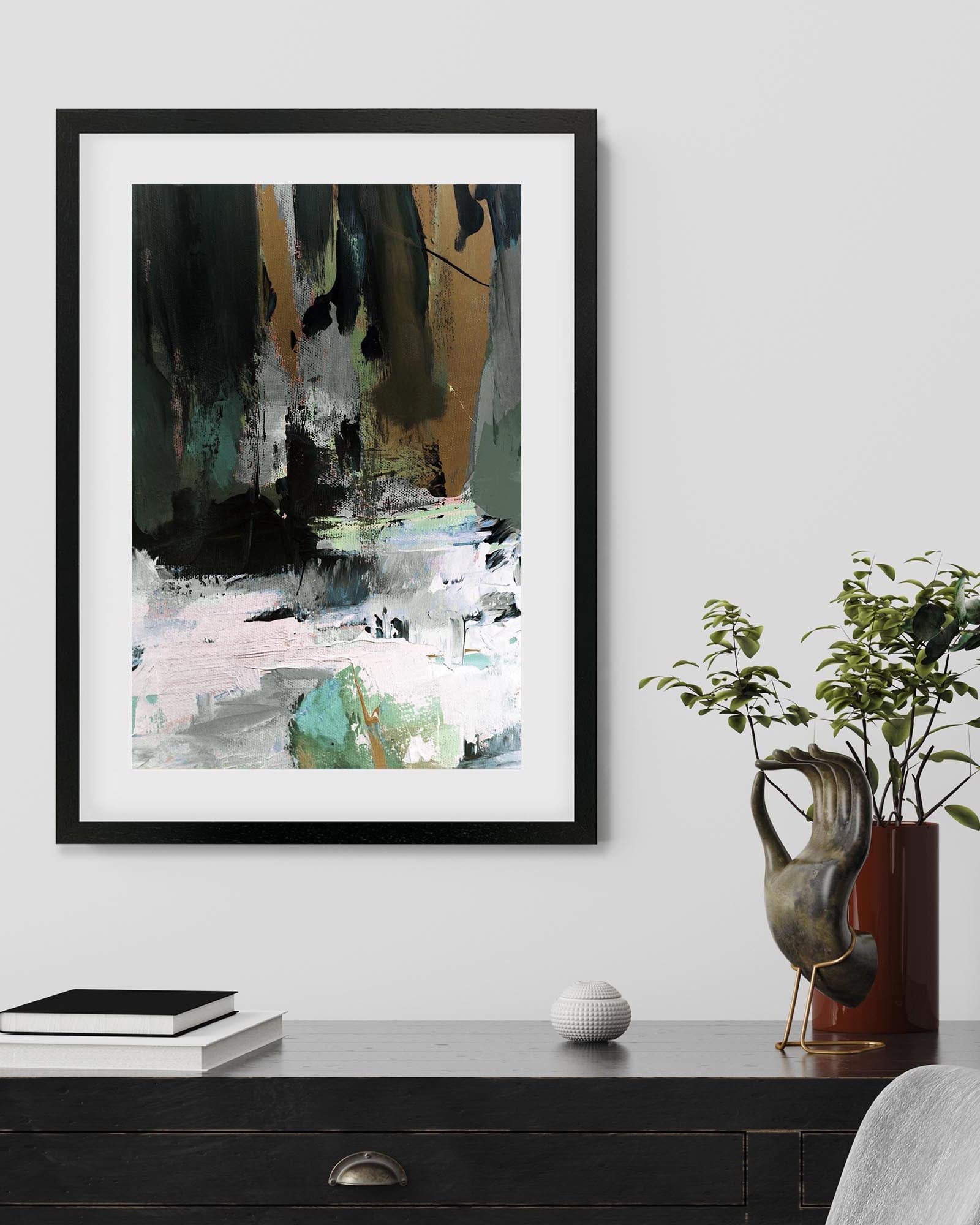 Framed abstract art piece on a wall above a wooden desk with decorative items.