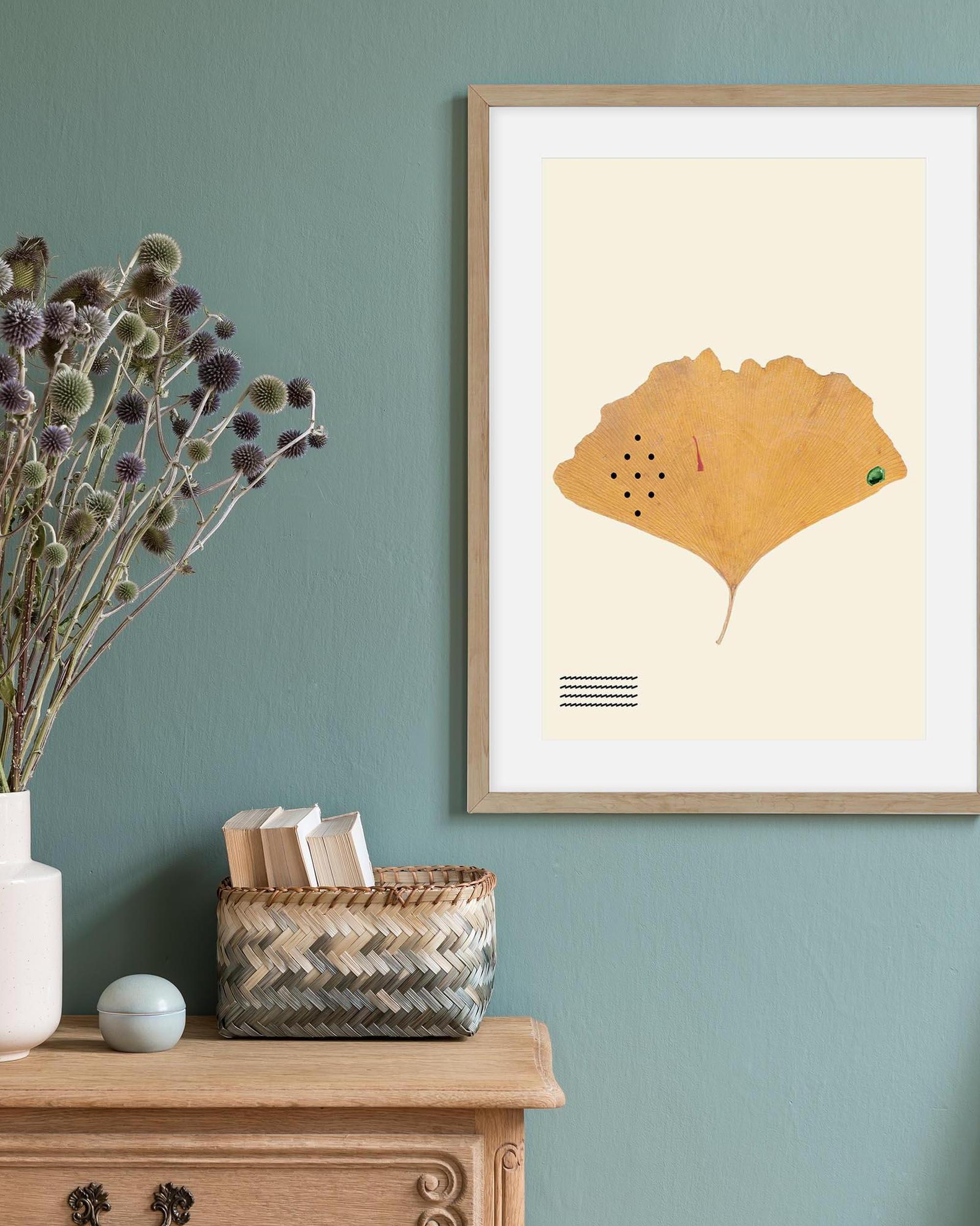 Framed artwork of a leaf on a wall with a wooden cabinet and decorative items.