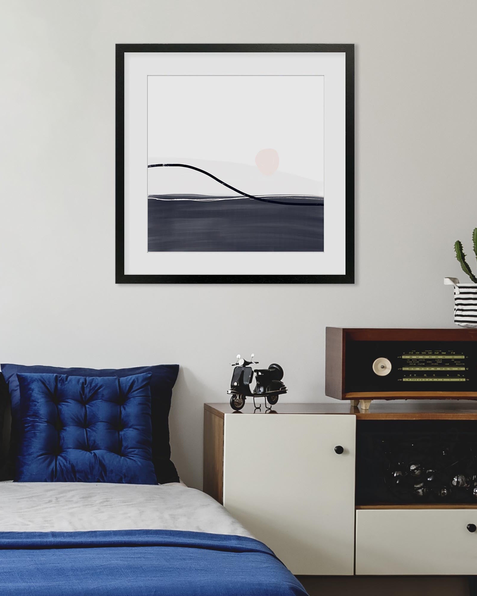 Framed abstract art above a bed with blue bedding in a bedroom setting.