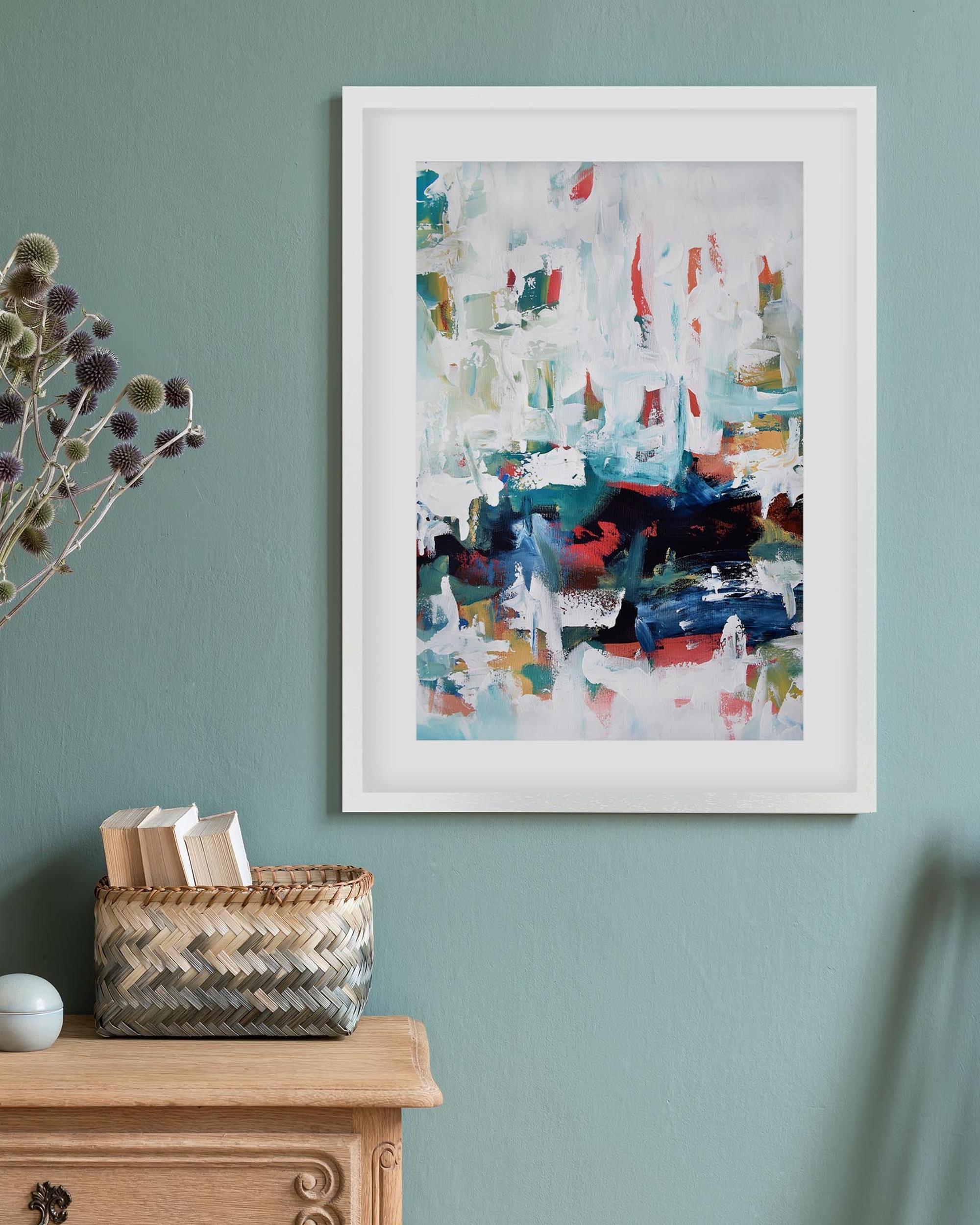 Framed abstract art on a wall with a wooden cabinet and basket below.