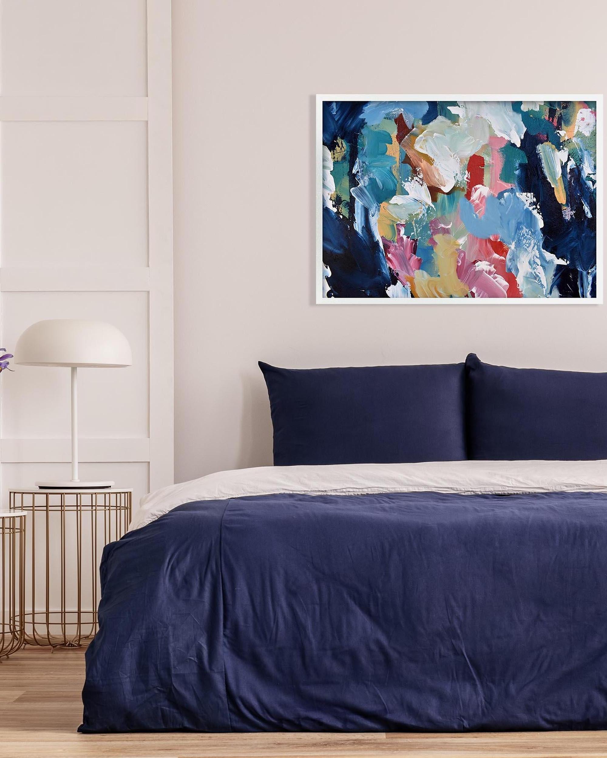 Bedroom with navy bedding, abstract art on the wall, and a lamp.