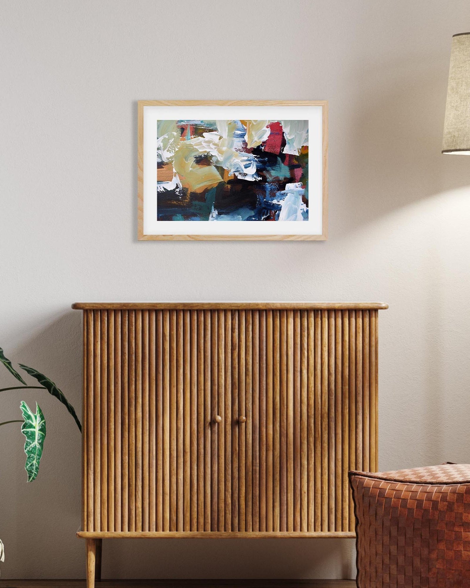 Wooden cabinet with a framed abstract painting above it on a wall.