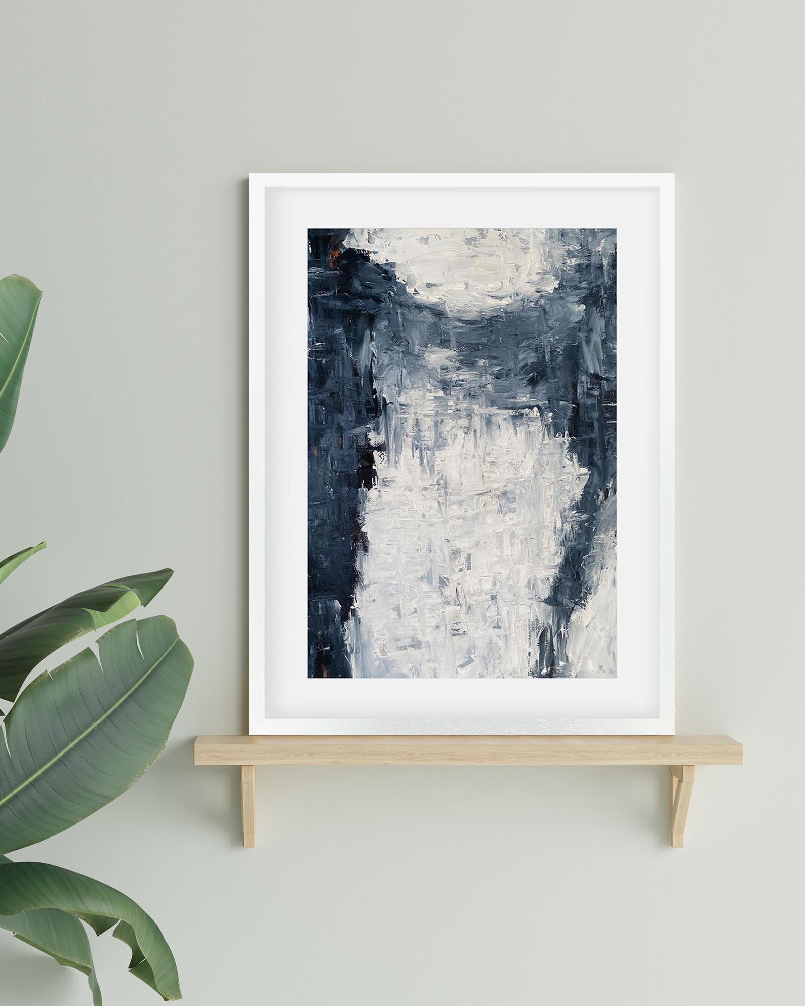 Framed abstract art print on a wooden shelf with a plant in the corner