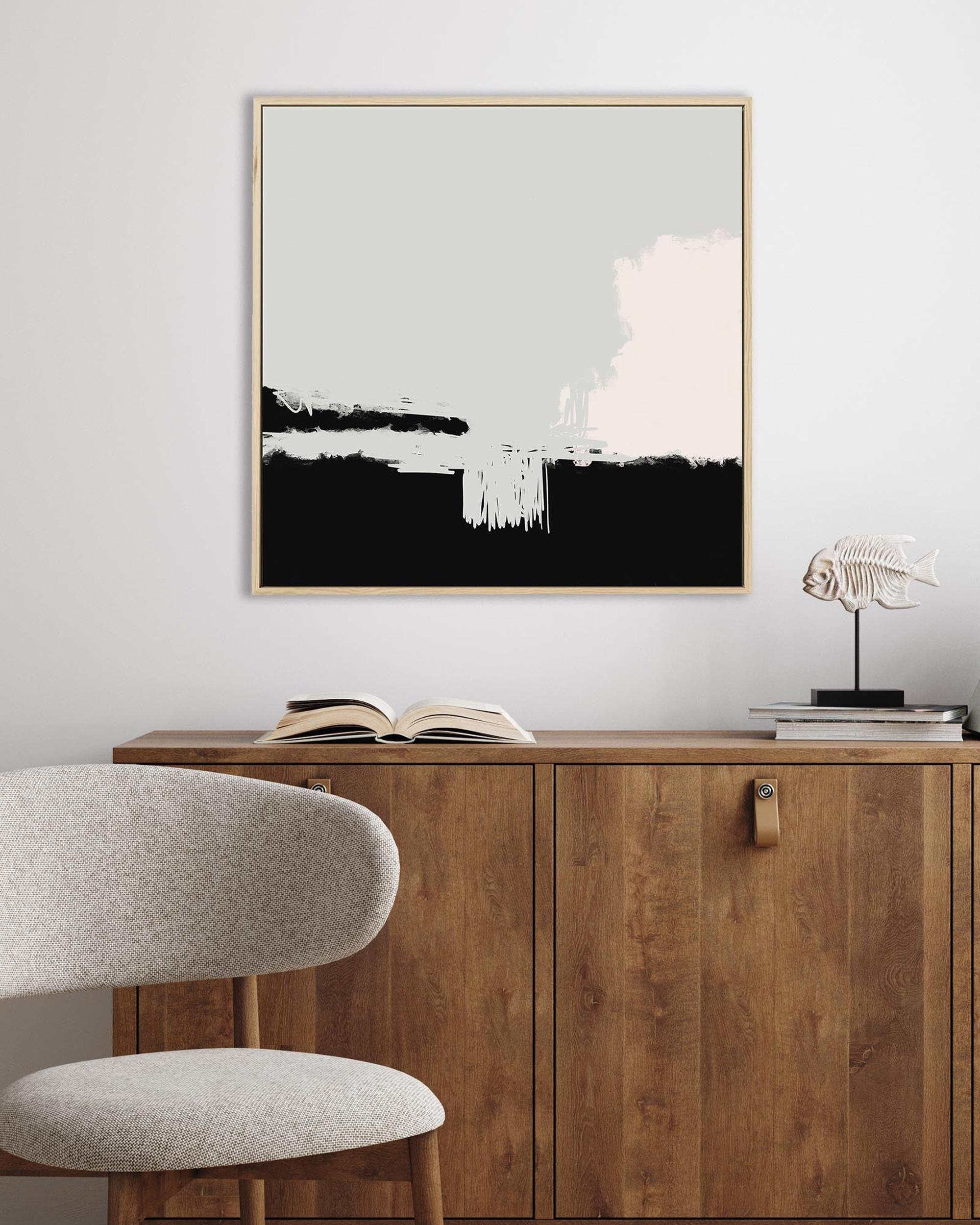 Abstract art piece on a wall above a wooden cabinet with a chair and books.