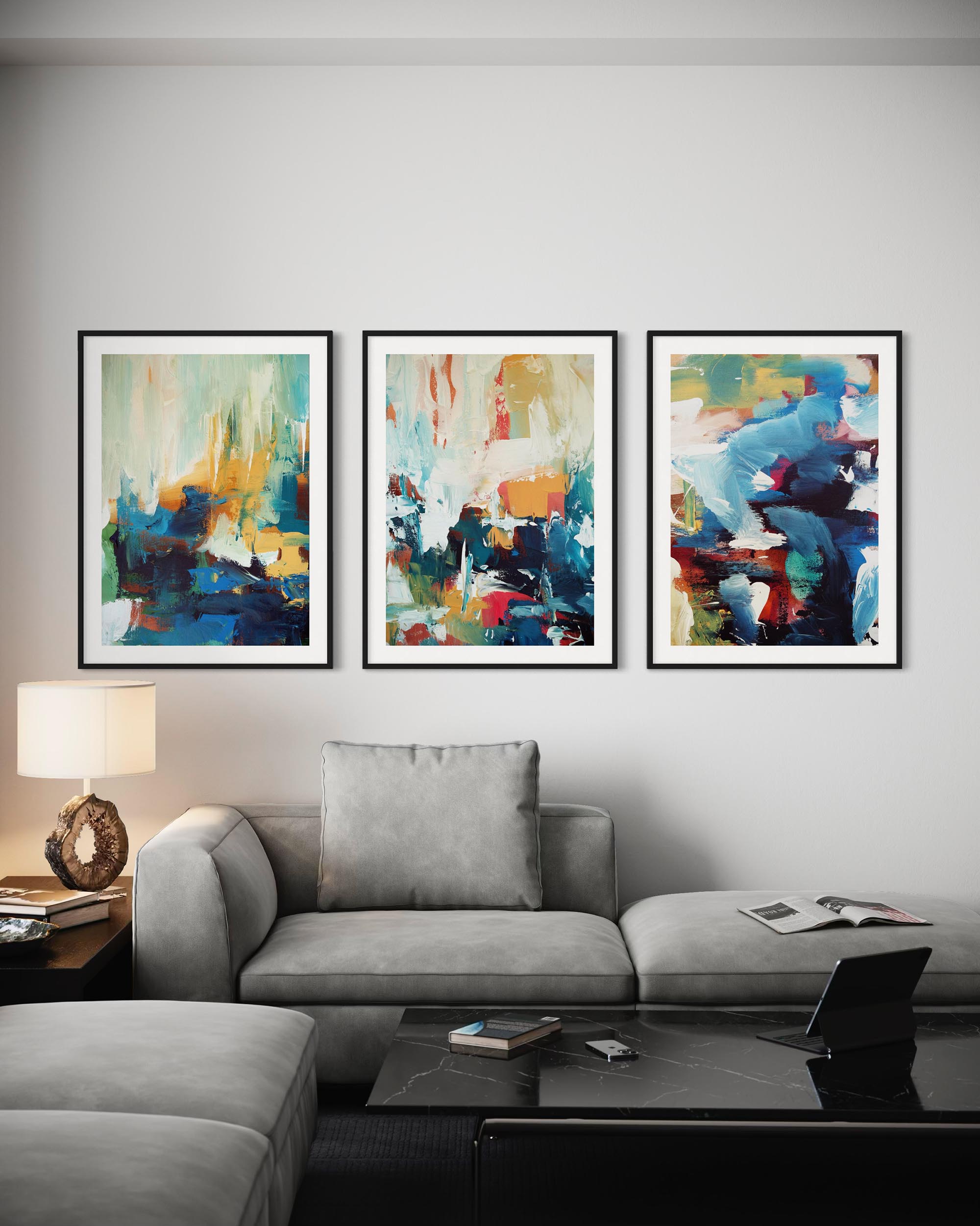 Three abstract paintings above a gray sofa in a living room setting.