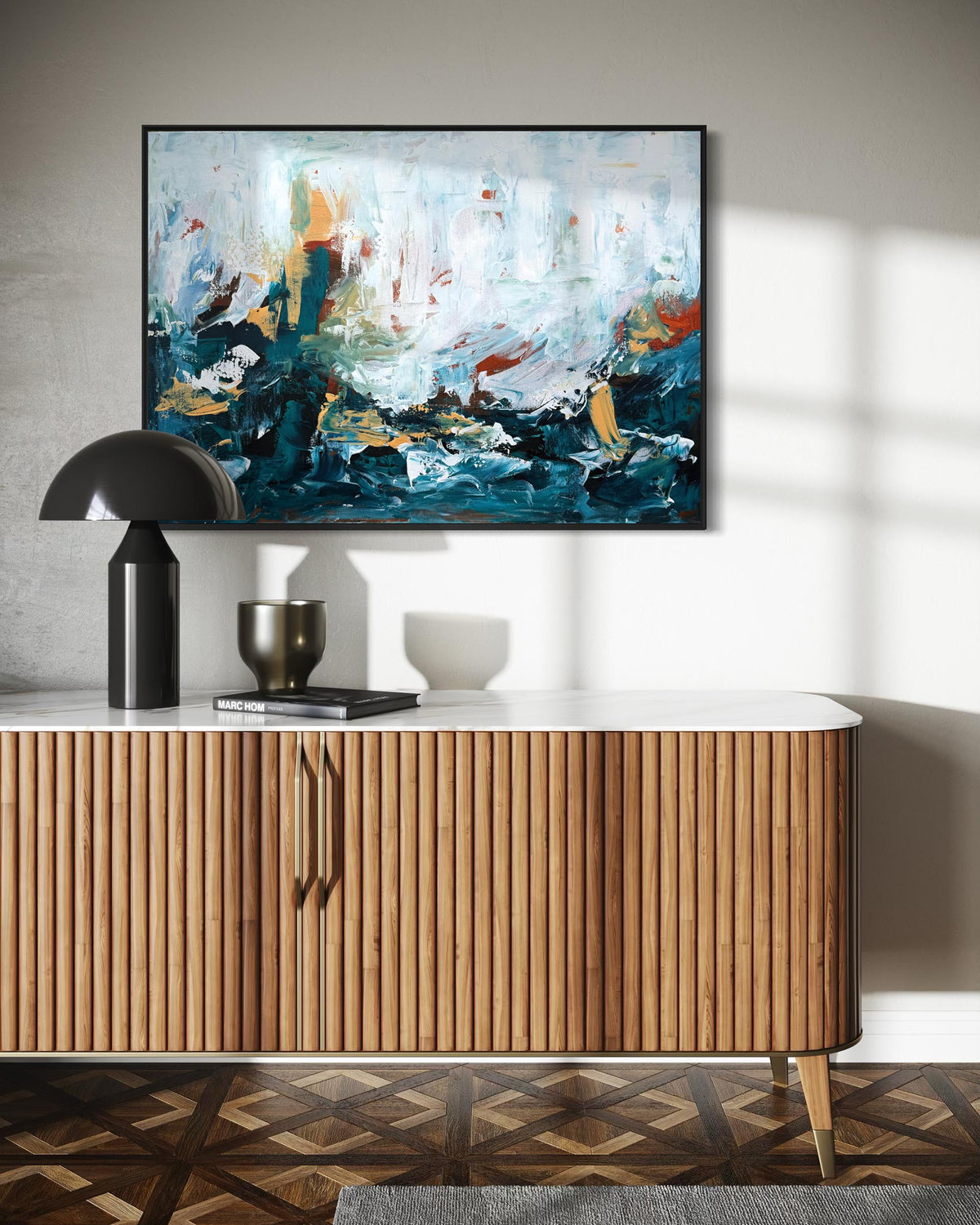 An abstract canvas painting with blue, white, and orange brushstrokes hanging on a light gray wall above a mid-century modern wooden credenza with a black dome lamp and decorative objects.