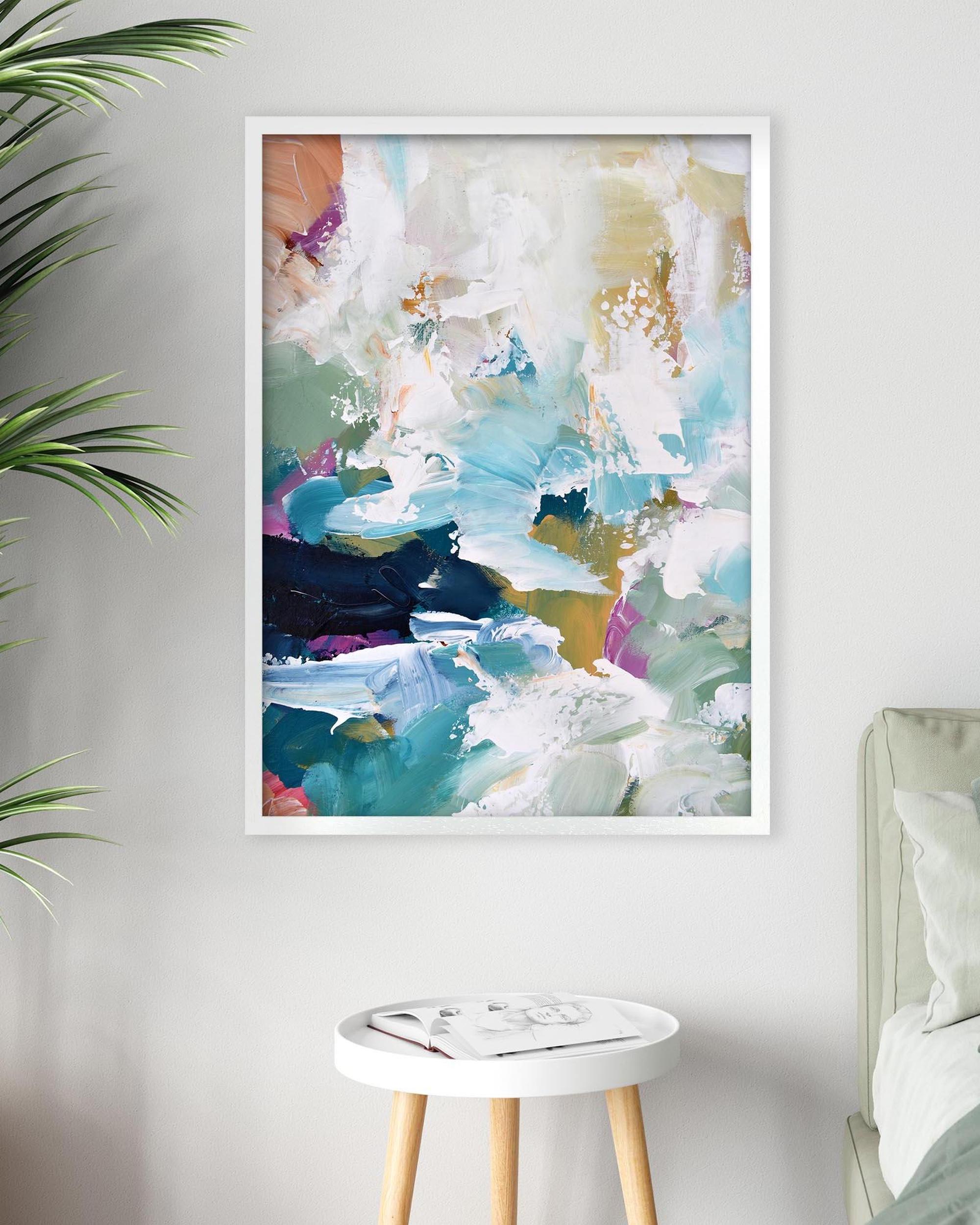 Framed abstract art print on a wall with a side table and plant in the foreground.