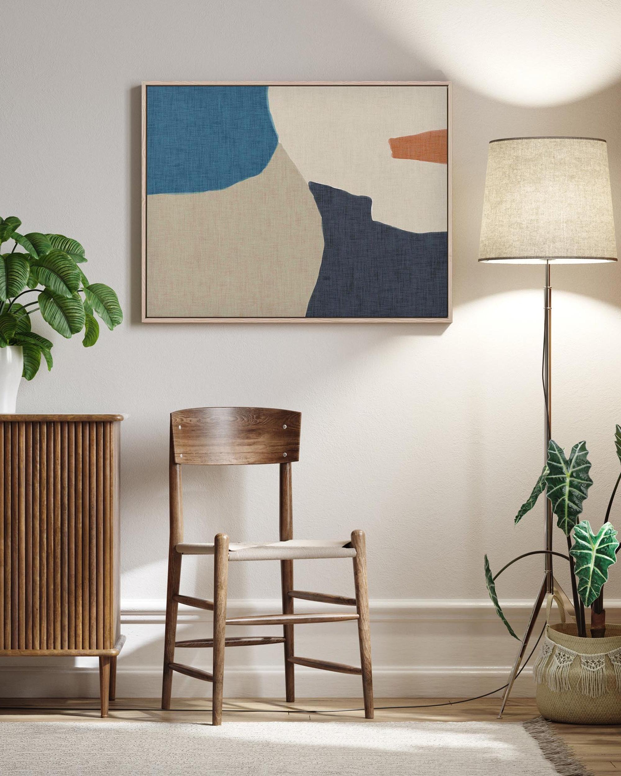 A framed canvas with an abstract design hanging on a wall, flanked by a floor lamp and a plant, with modern furniture in the setting.