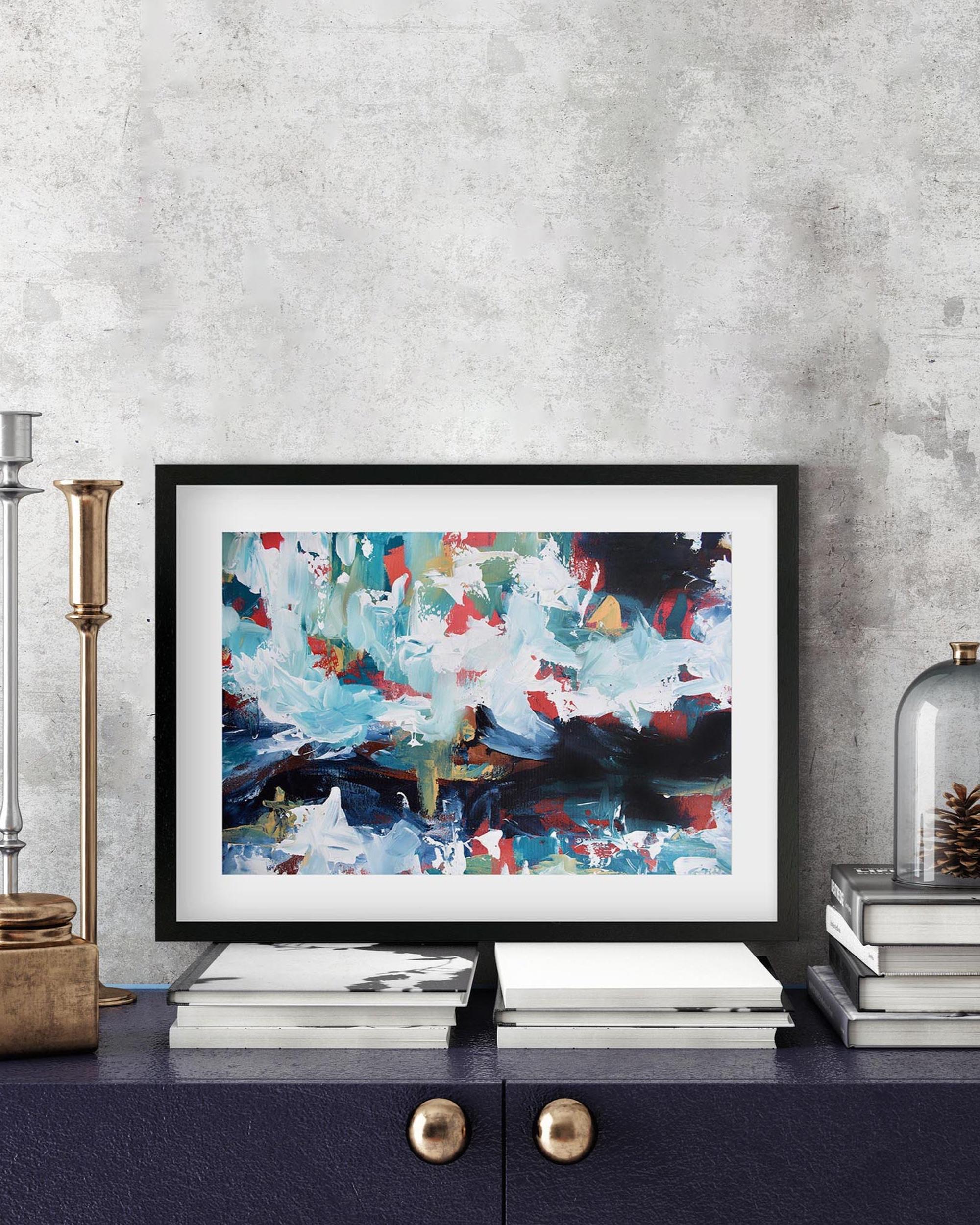 Framed abstract art piece on a shelf with decorative items against a gray wall.