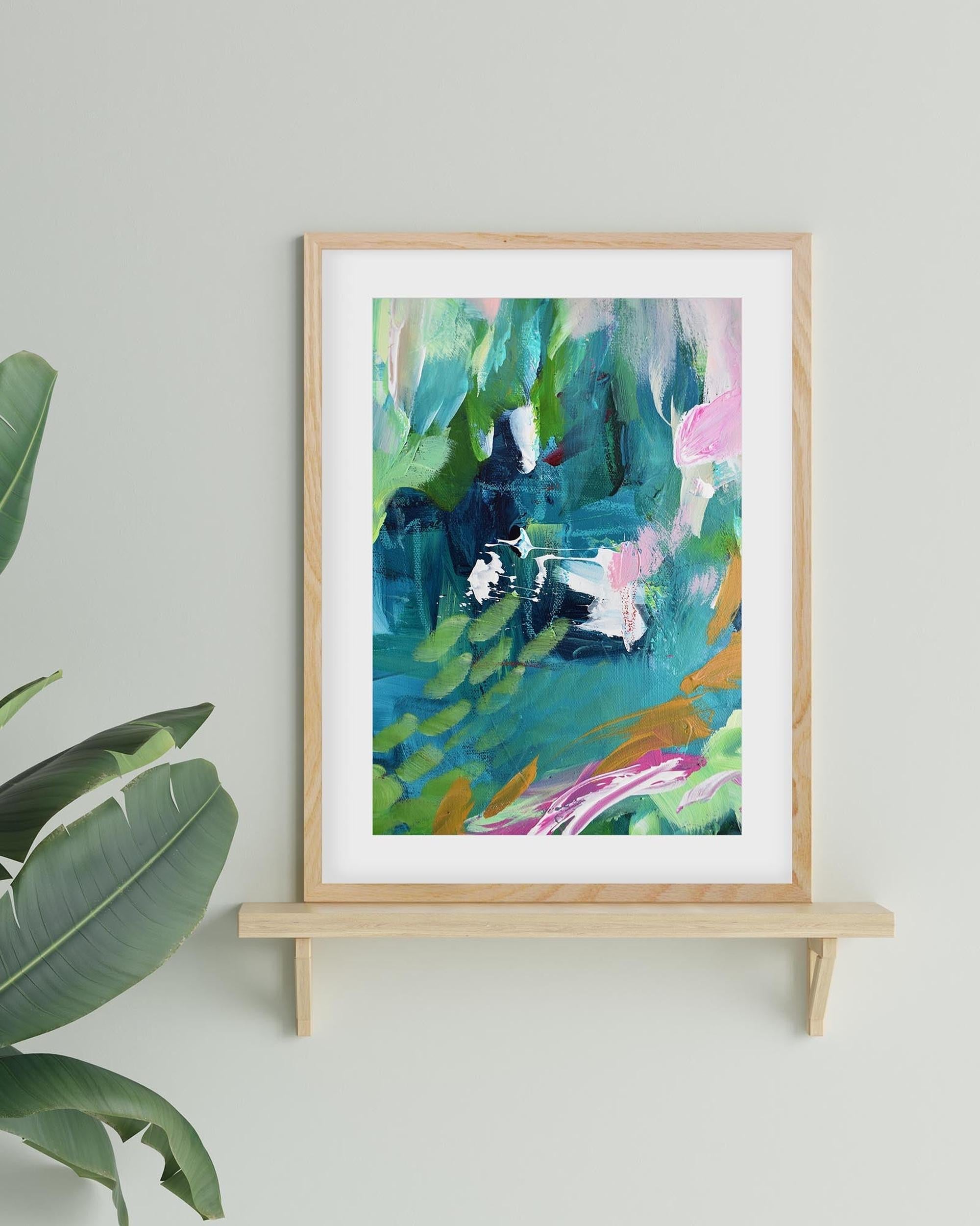 Framed abstract art print on a wooden shelf with a plant in the corner.