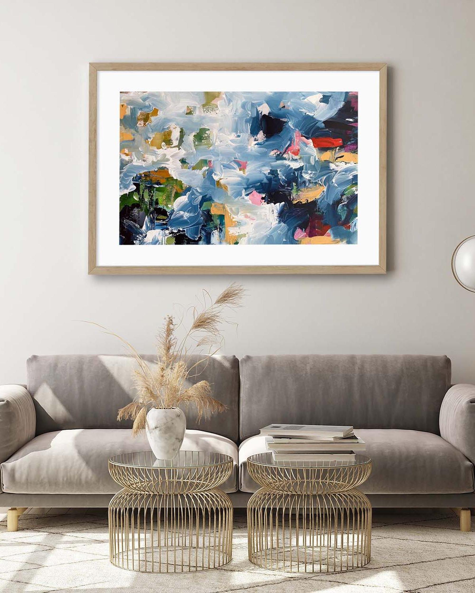 Abstract painting in a wooden frame above a gray sofa in a living room.