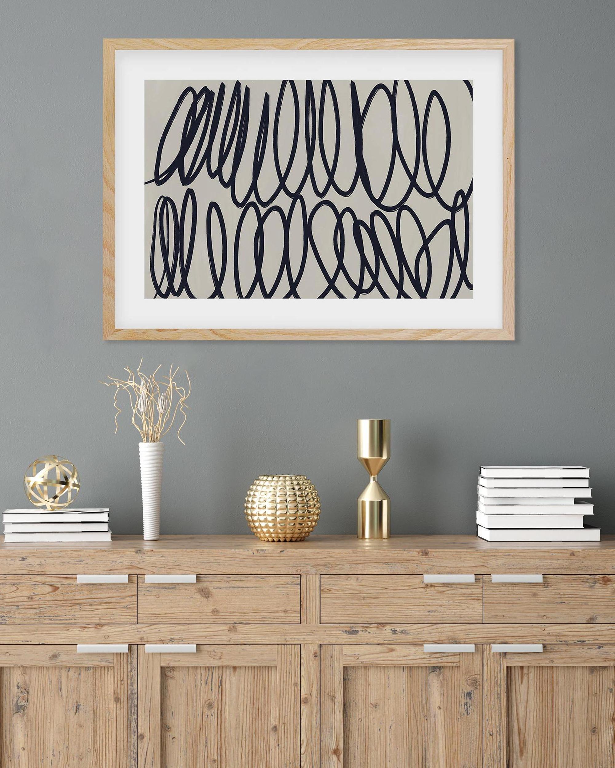 Framed abstract art above a wooden cabinet with decorative items on a gray wall.