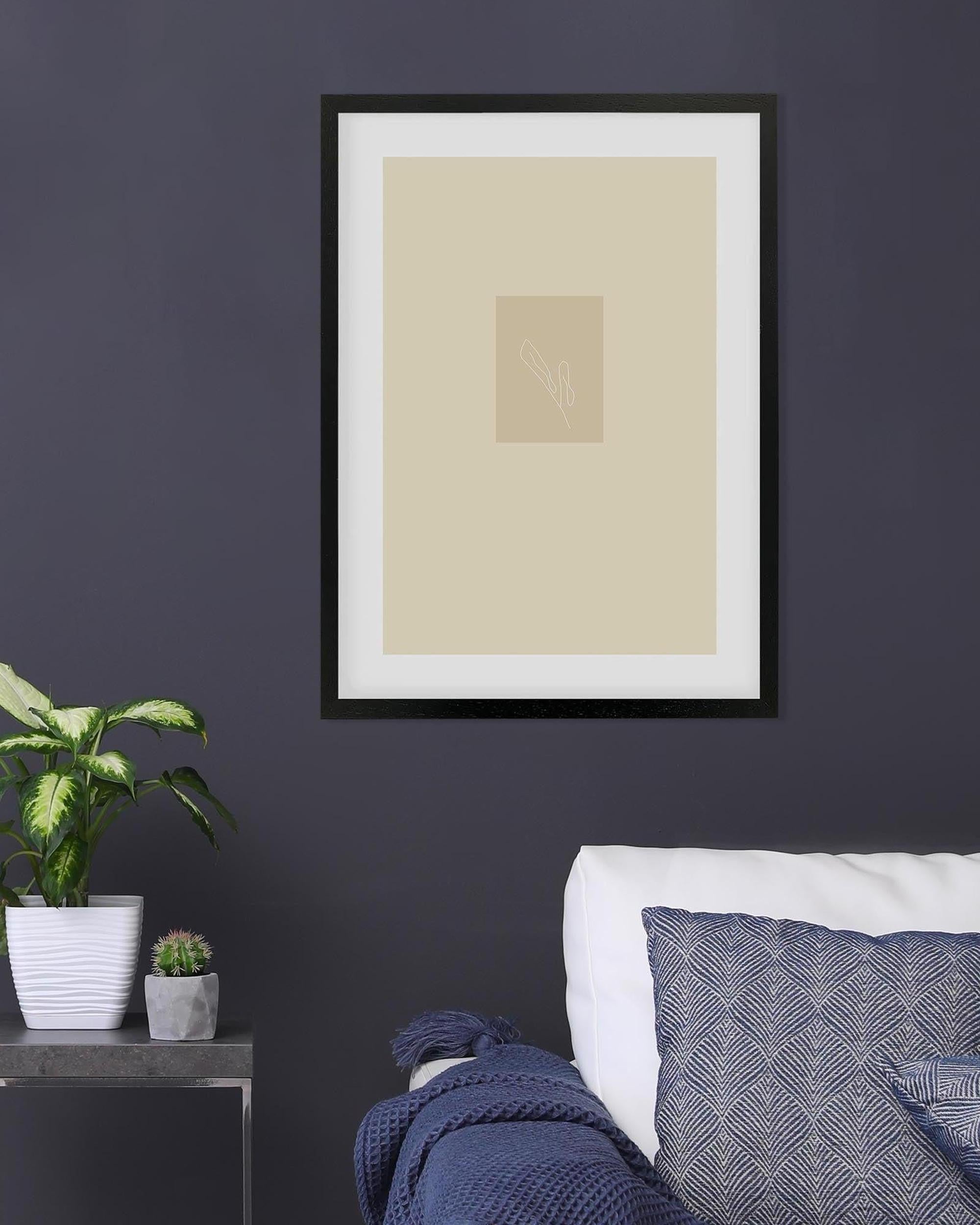 Framed beige art print on a dark wall with a plant and sofa in the foreground
