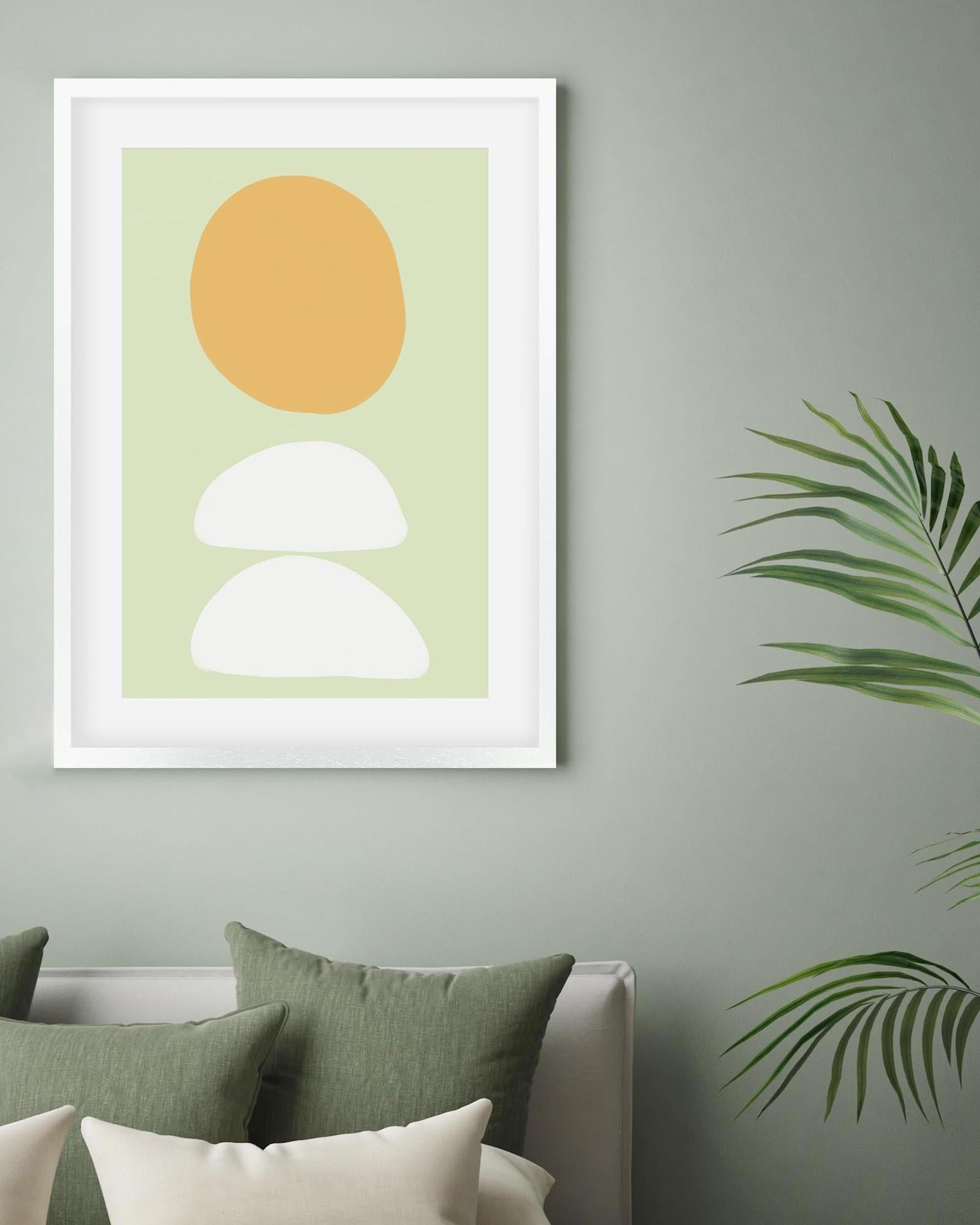 Framed abstract art print with a yellow circle and white shapes on a light green background, hanging on a wall.