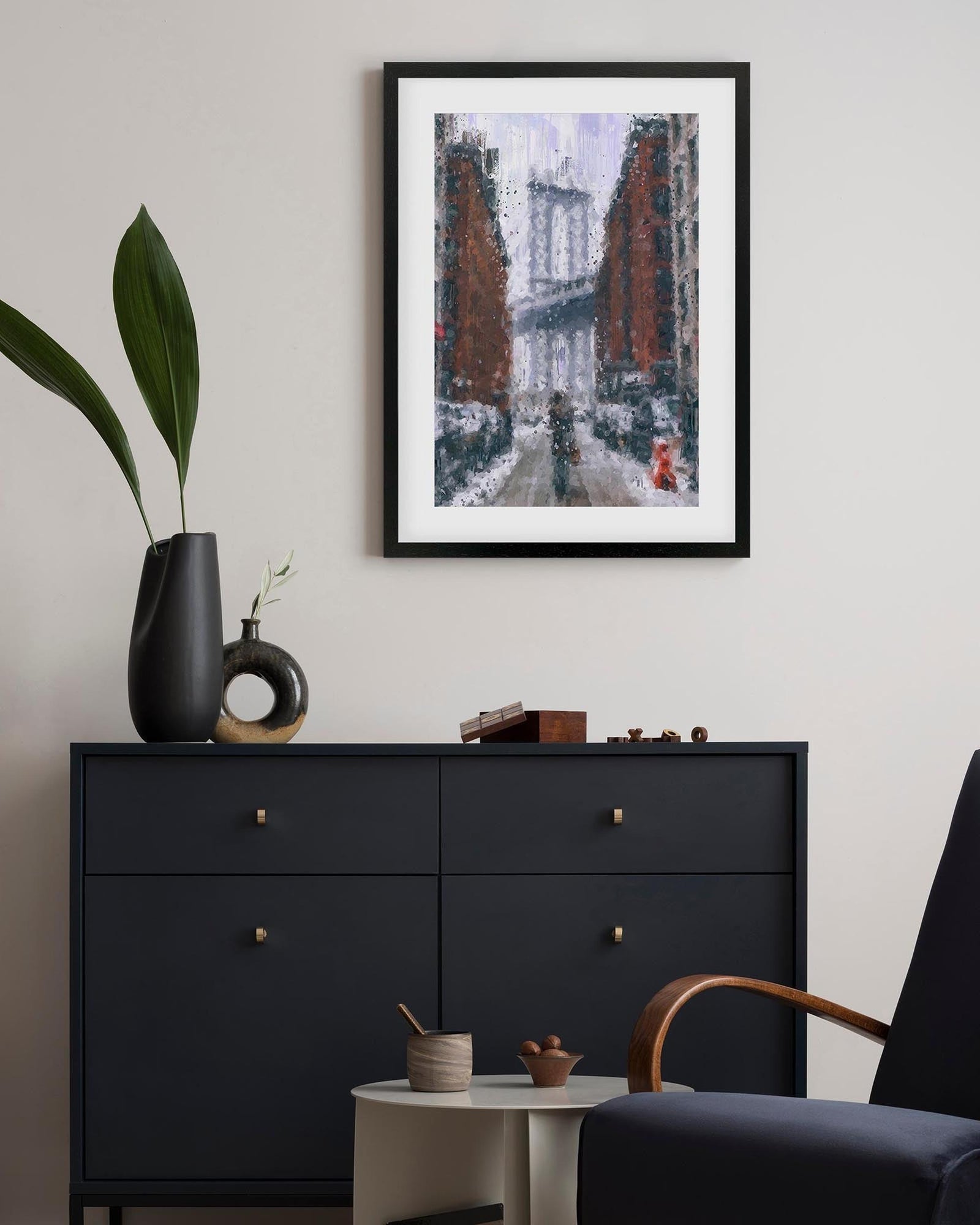 Framed artwork above a black dresser in a room with a plant and chair.