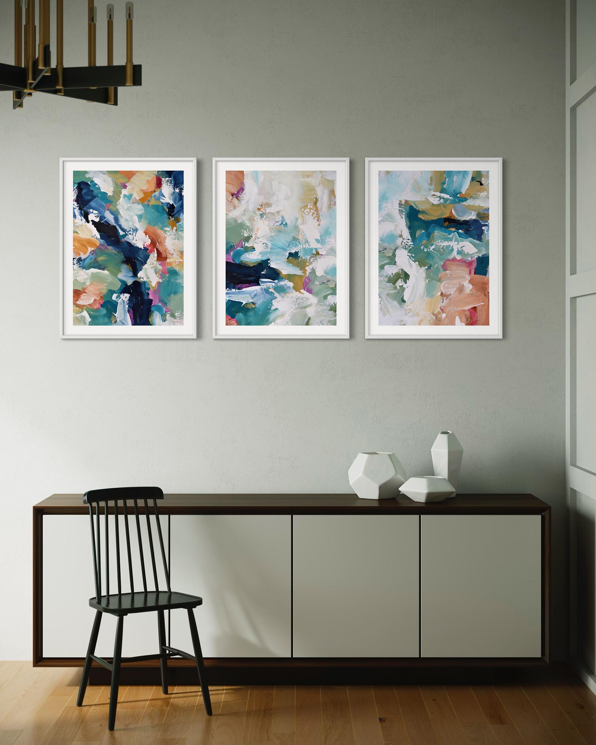 Three abstract paintings on a wall above a console table with a chair and decorative vases.