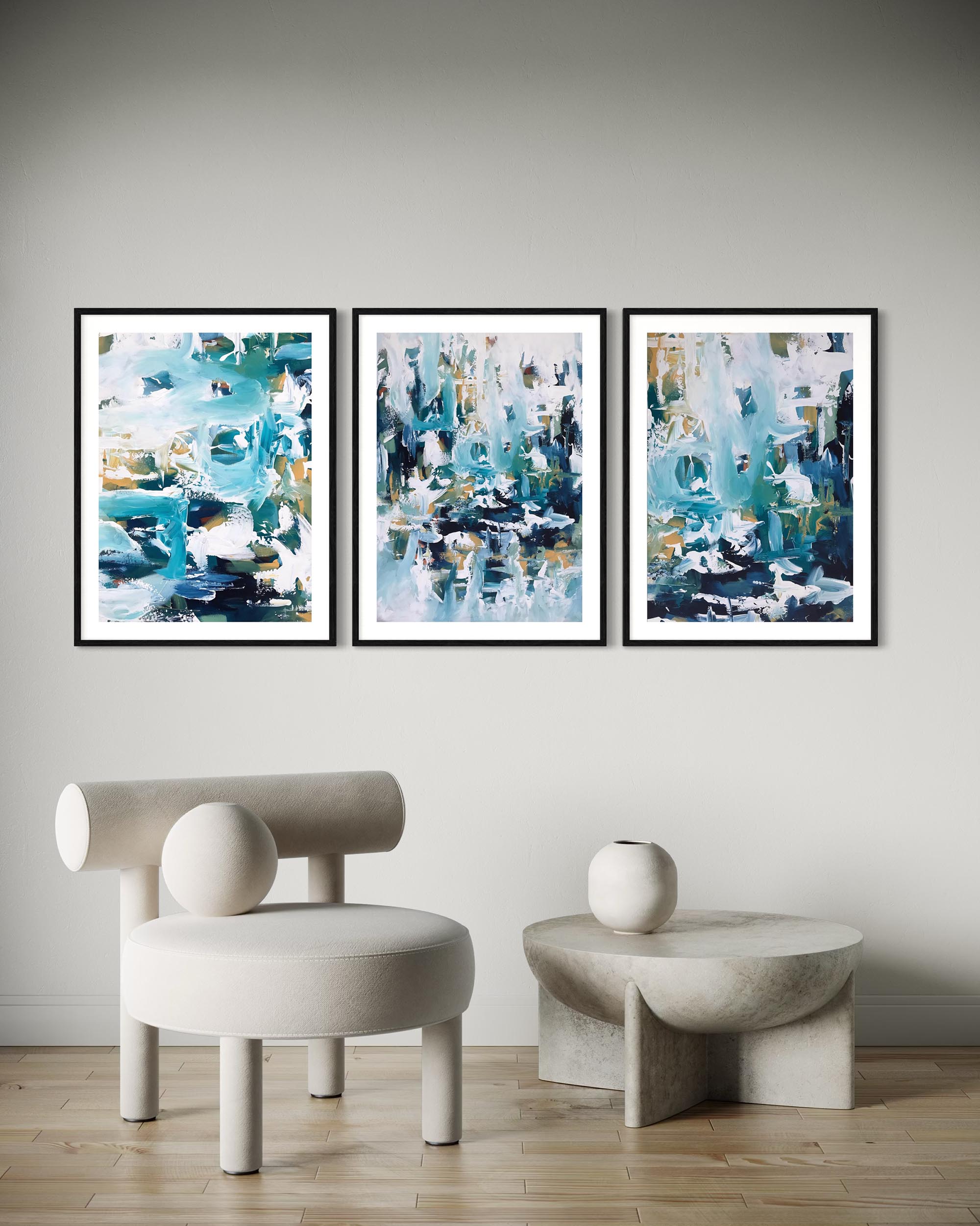 Three abstract paintings on a wall with a modern chair and table below.