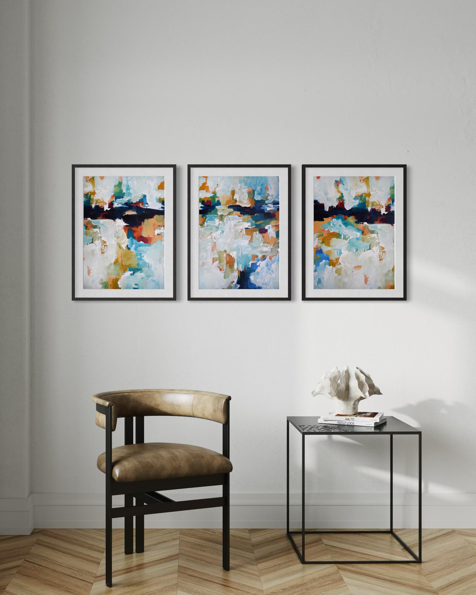 Three abstract paintings on a wall above a chair and small table.