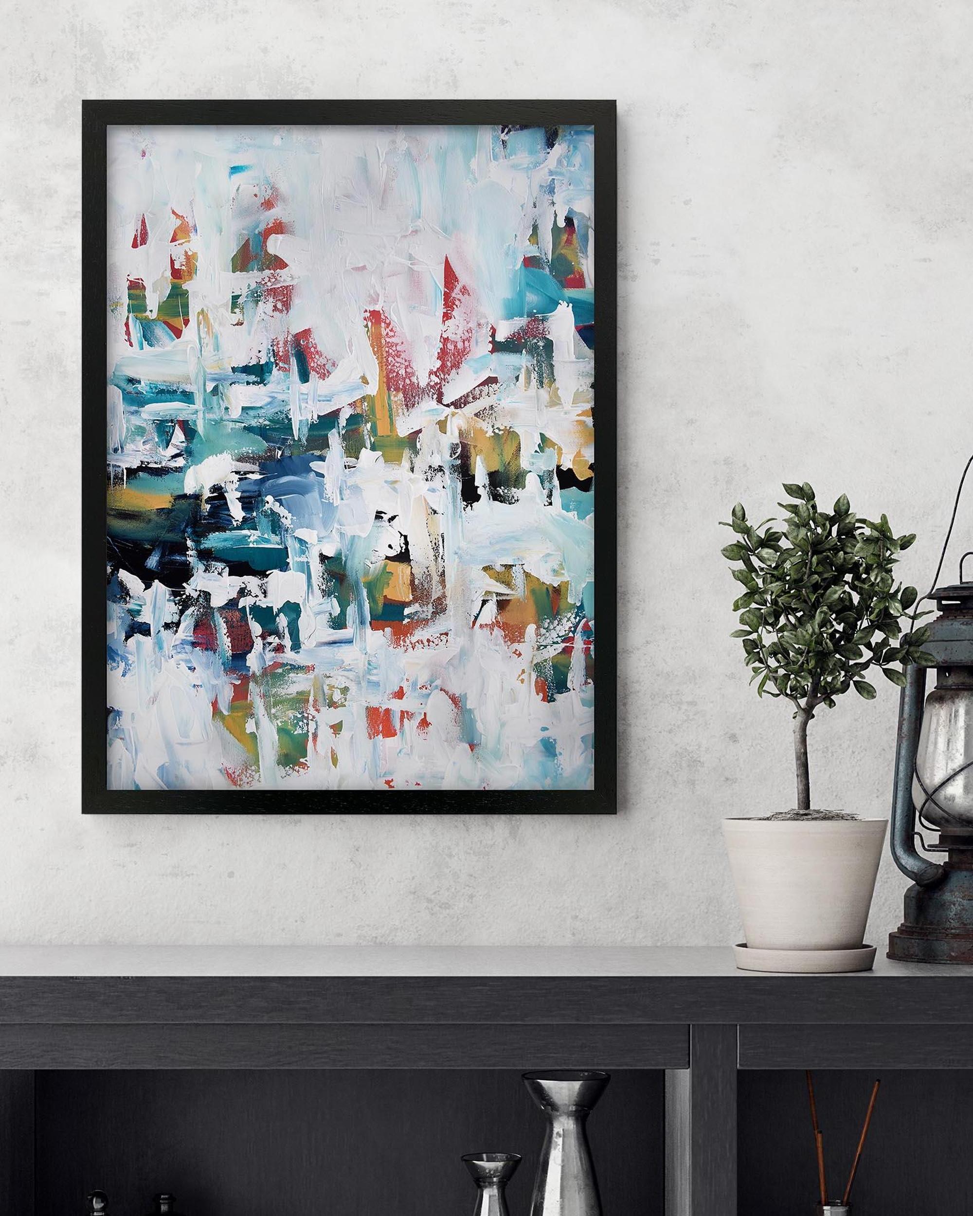 Framed abstract painting on a wall with a plant and lantern below.