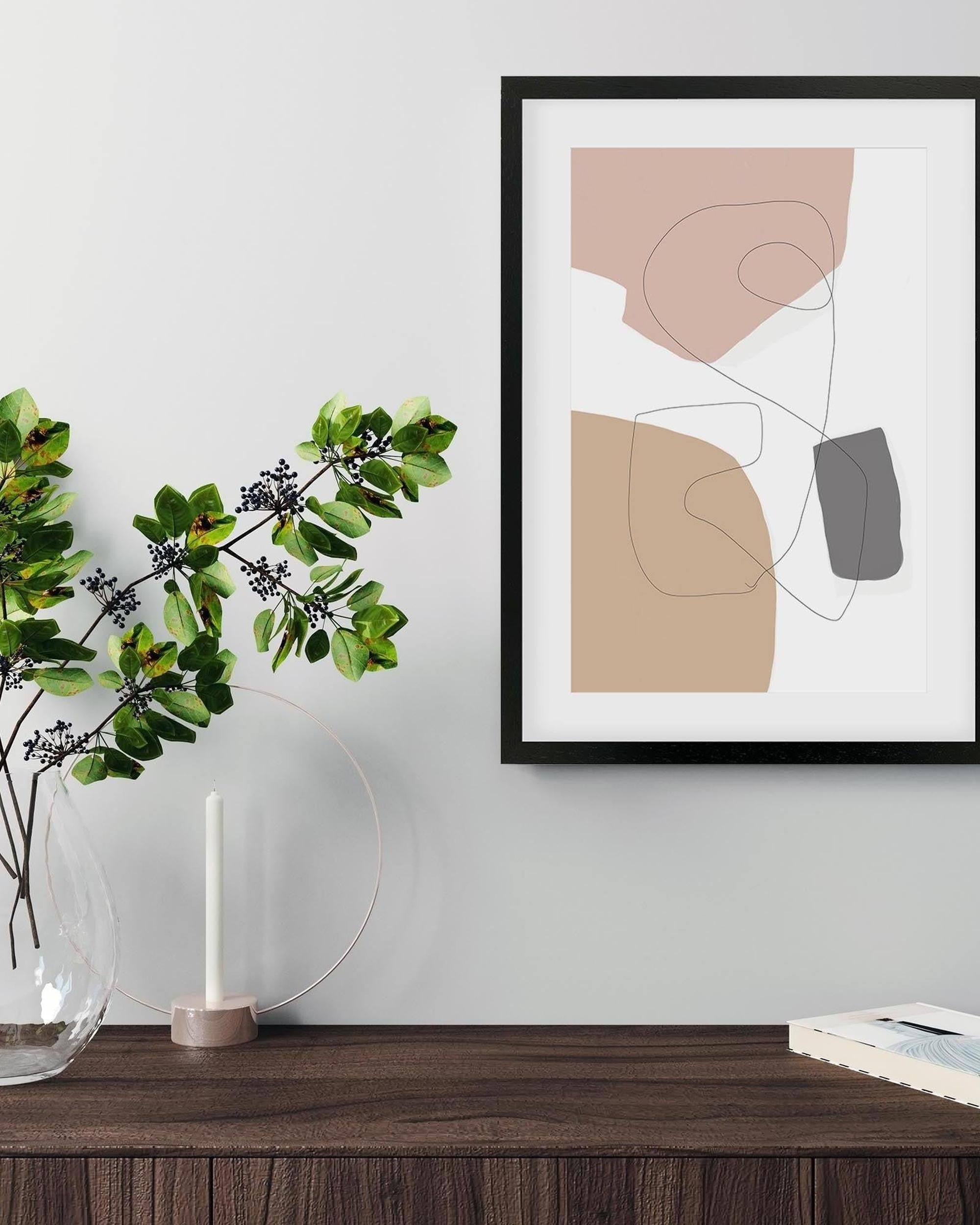 Abstract art print in a black frame on a wall above a wooden surface with a vase and plant.
