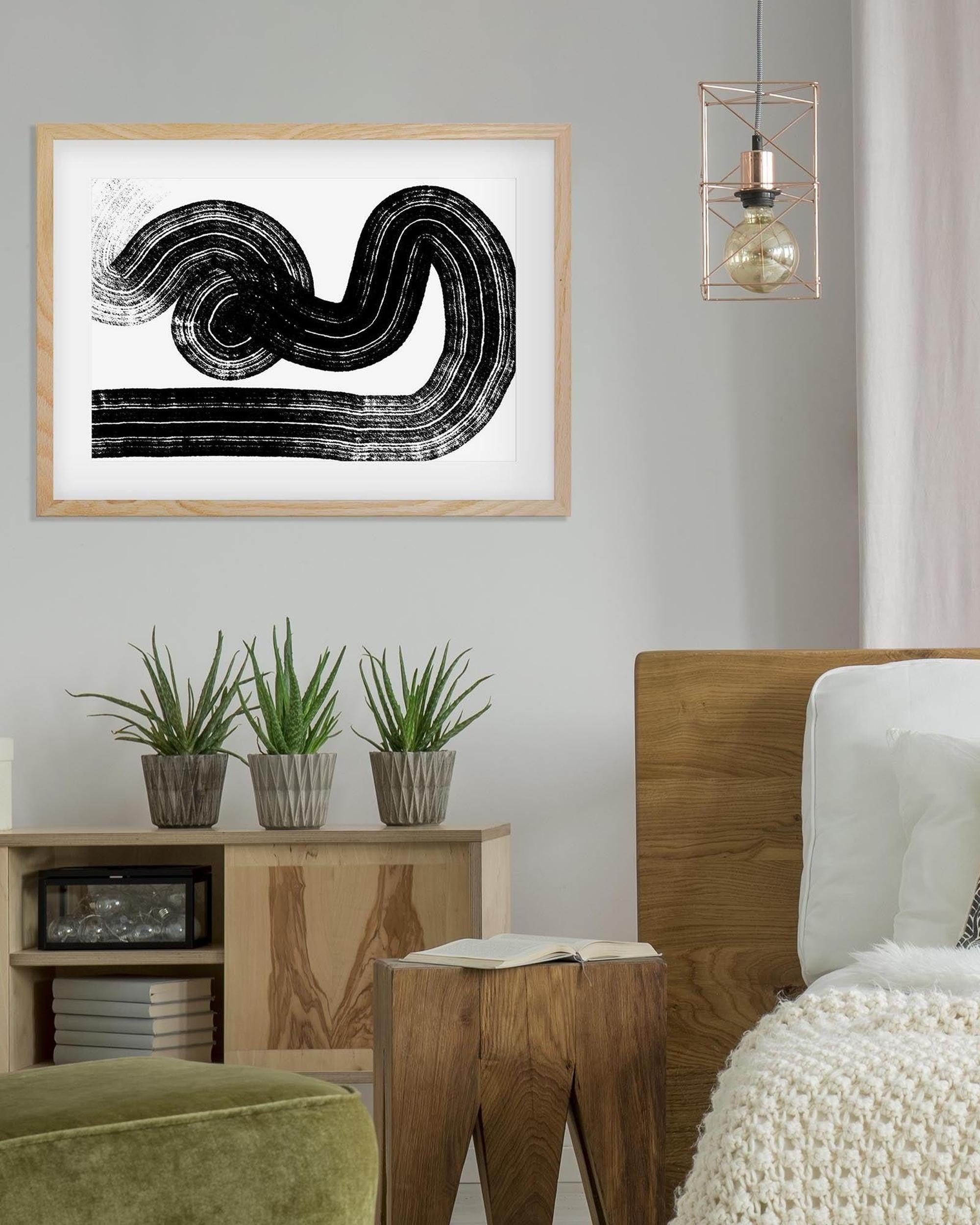 Framed abstract artwork on a wall with a wooden side table and plants in a living room setting.