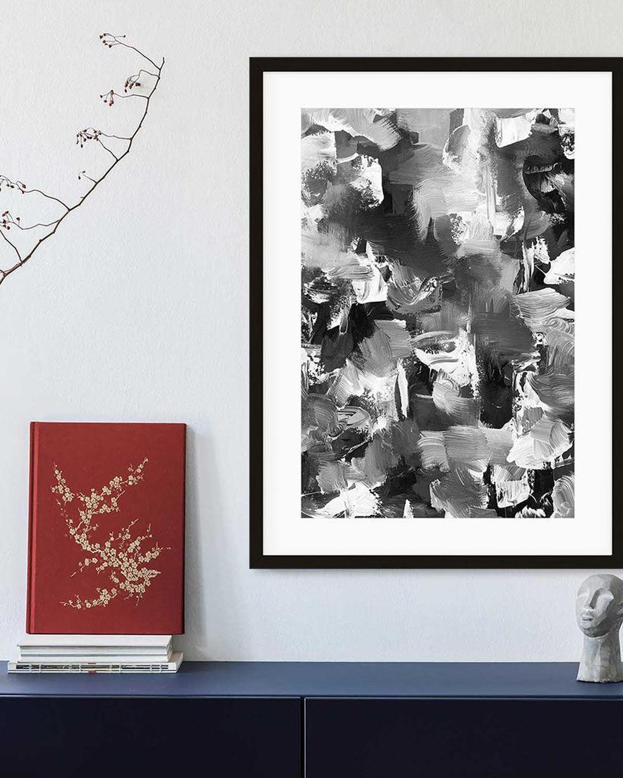 Framed abstract art piece on a wall with a red book and sculpture below.