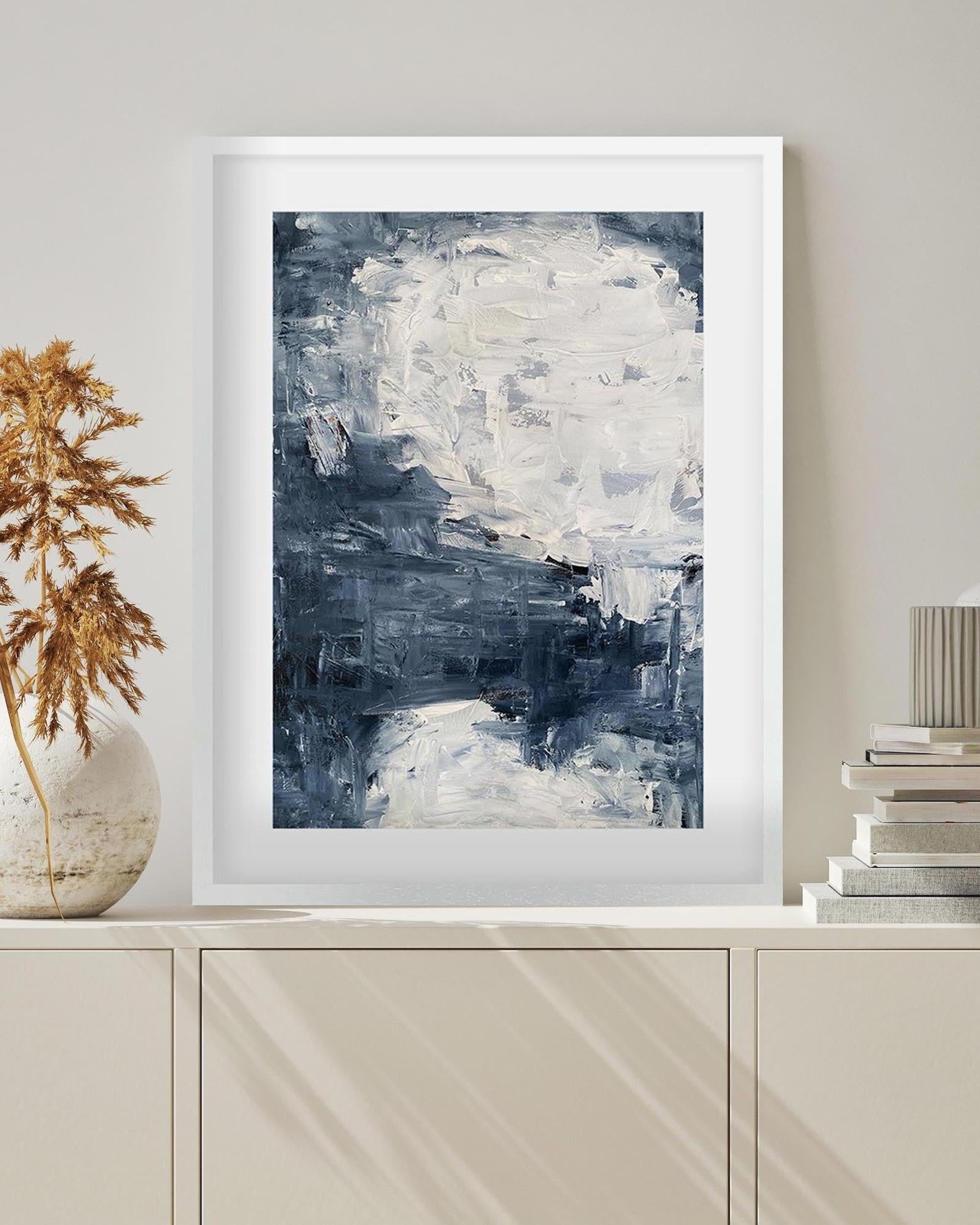 Abstract painting in a white frame on a wall above a cabinet with decorative items.