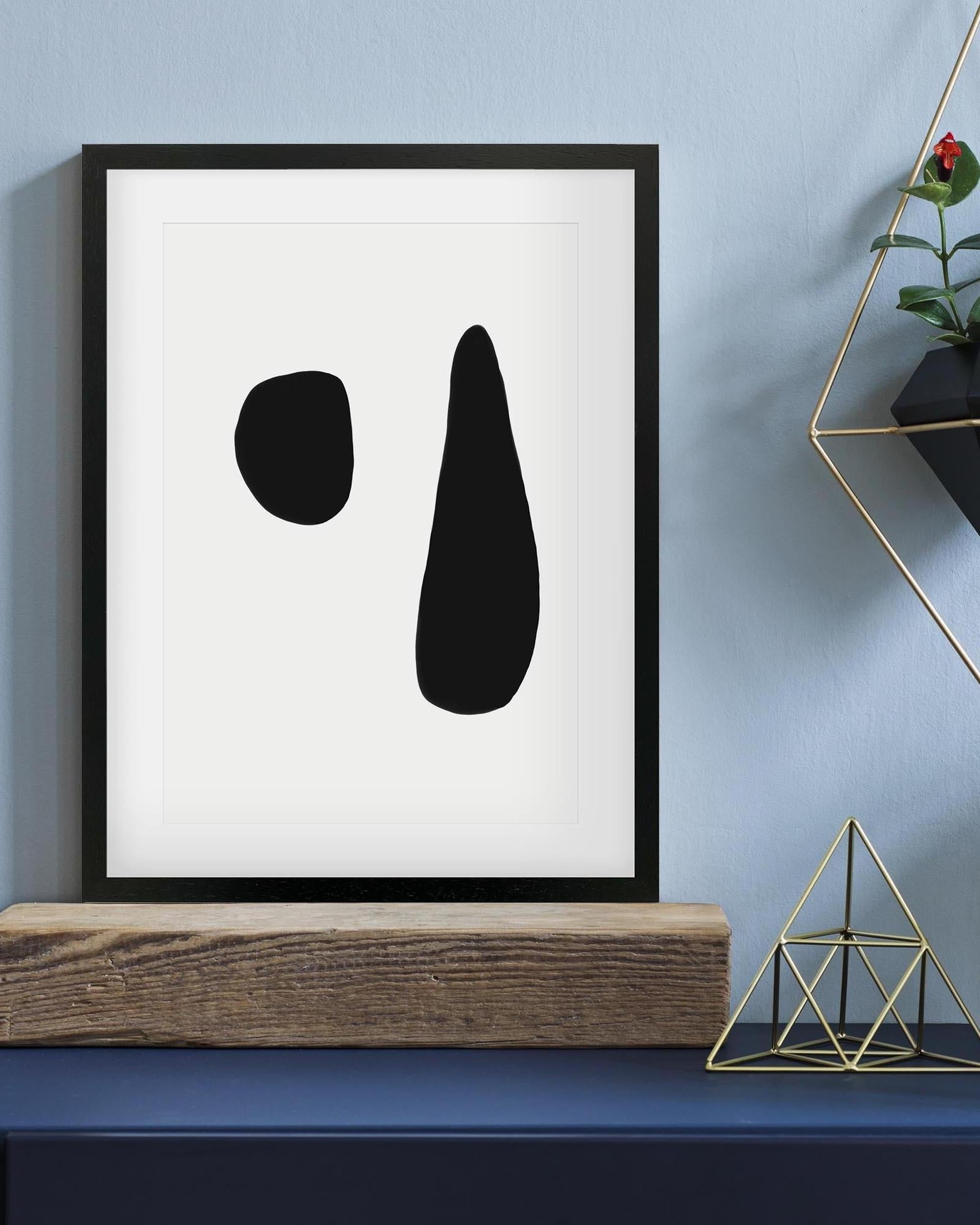 Framed abstract art with black shapes on a white background, displayed on a shelf against a blue wall.