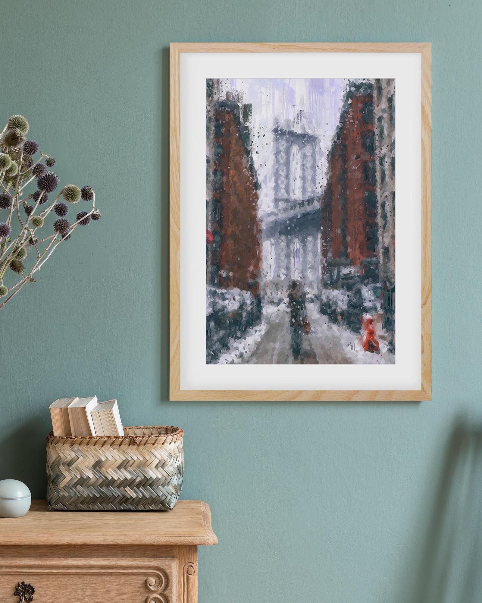 Framed abstract artwork on a teal wall with a wooden cabinet and basket below.