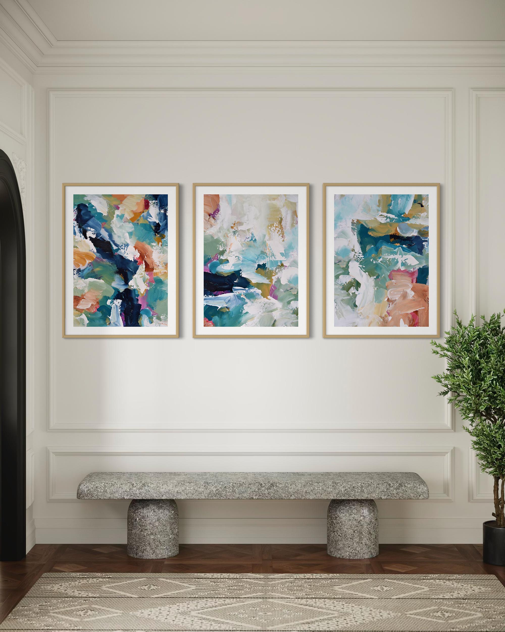 Three abstract art pieces on a wall above a stone bench in a room.
