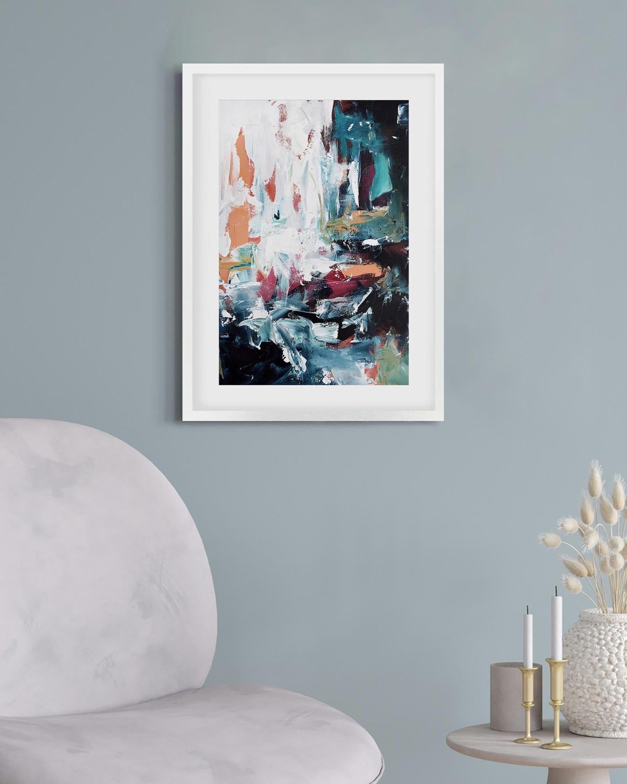 Abstract painting in a white frame on a gray wall above a chair and side table with decorative items.