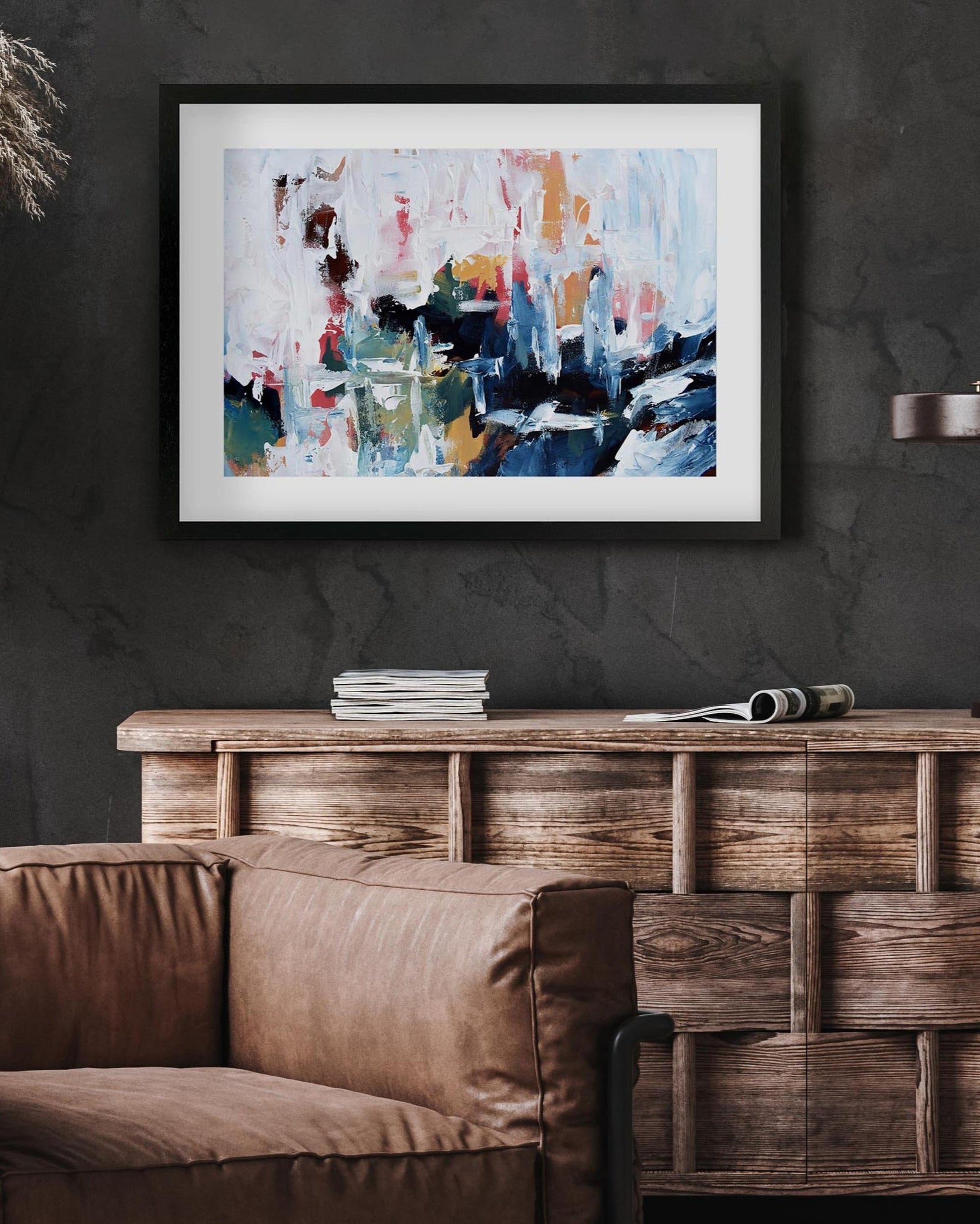 Abstract art piece on a dark wall above a brown sofa and wooden cabinet.