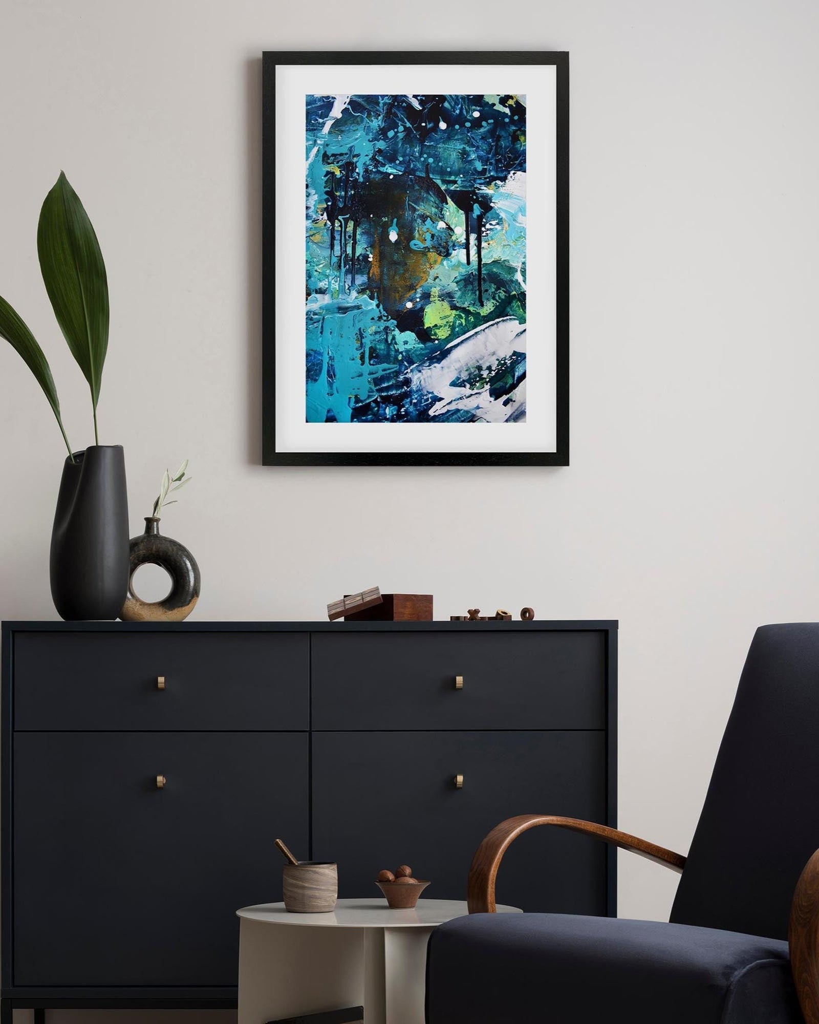 Modern interior with a black dresser, plant, and abstract artwork on a white wall.