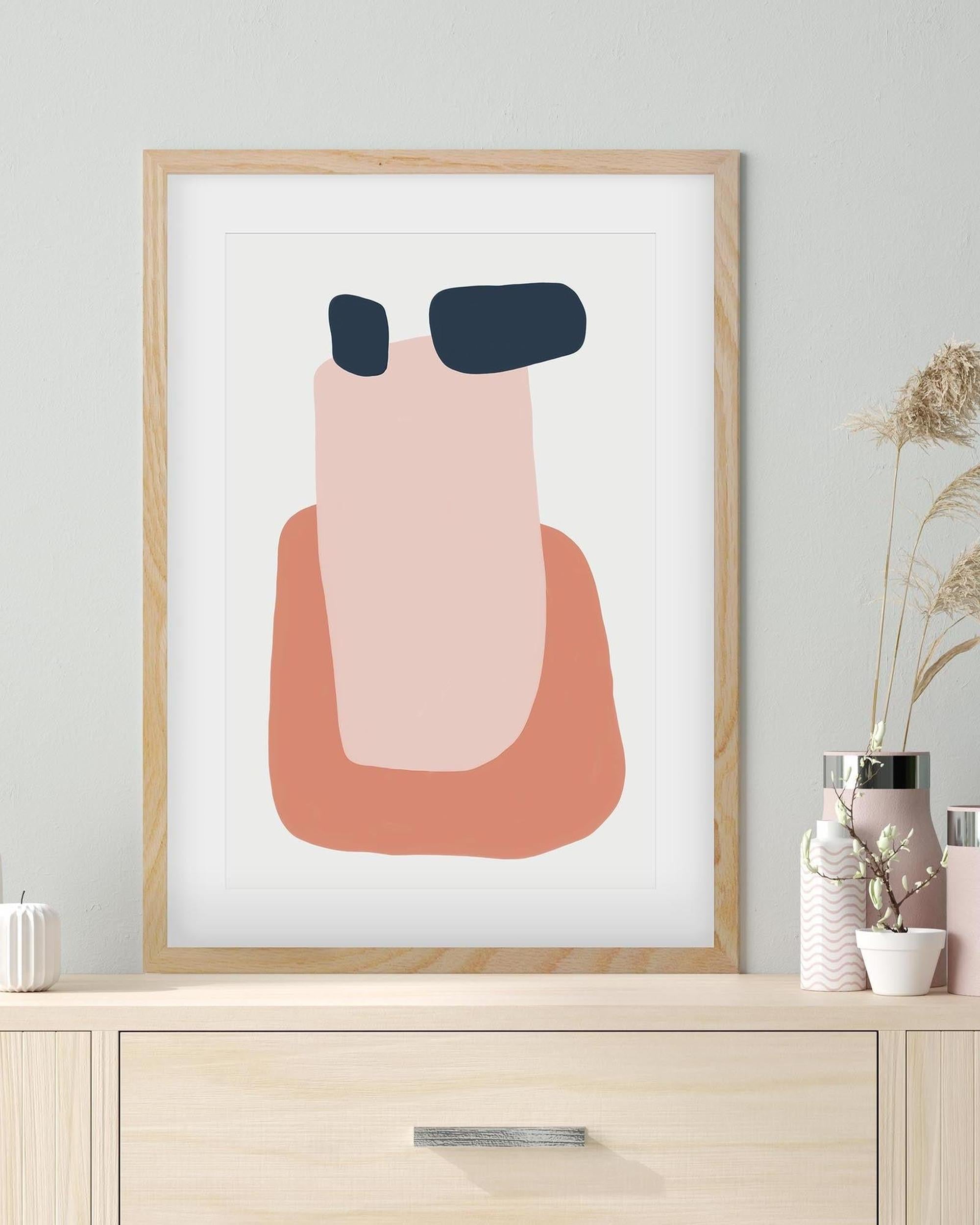 Framed abstract art print with pink and blue shapes on a white background, displayed on a wooden shelf.