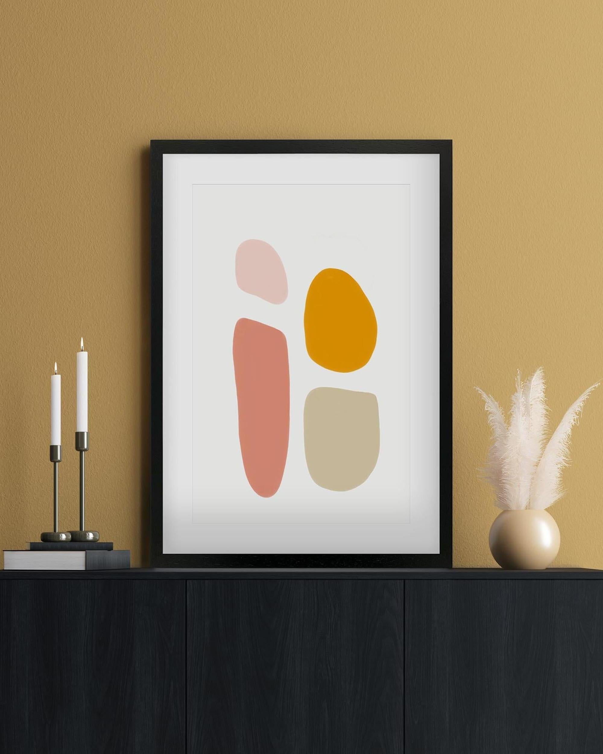 Framed abstract art print with colorful shapes on a beige wall.