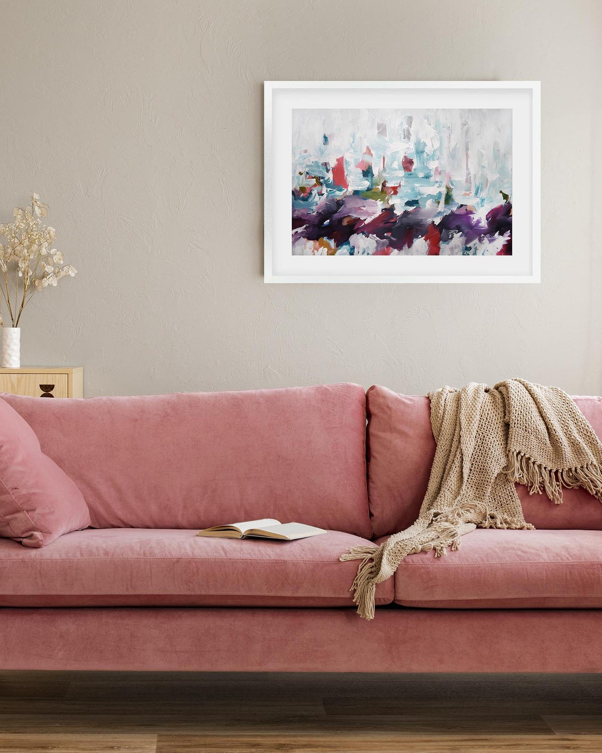 Pink sofa in a living room with a colorful abstract painting on the wall.