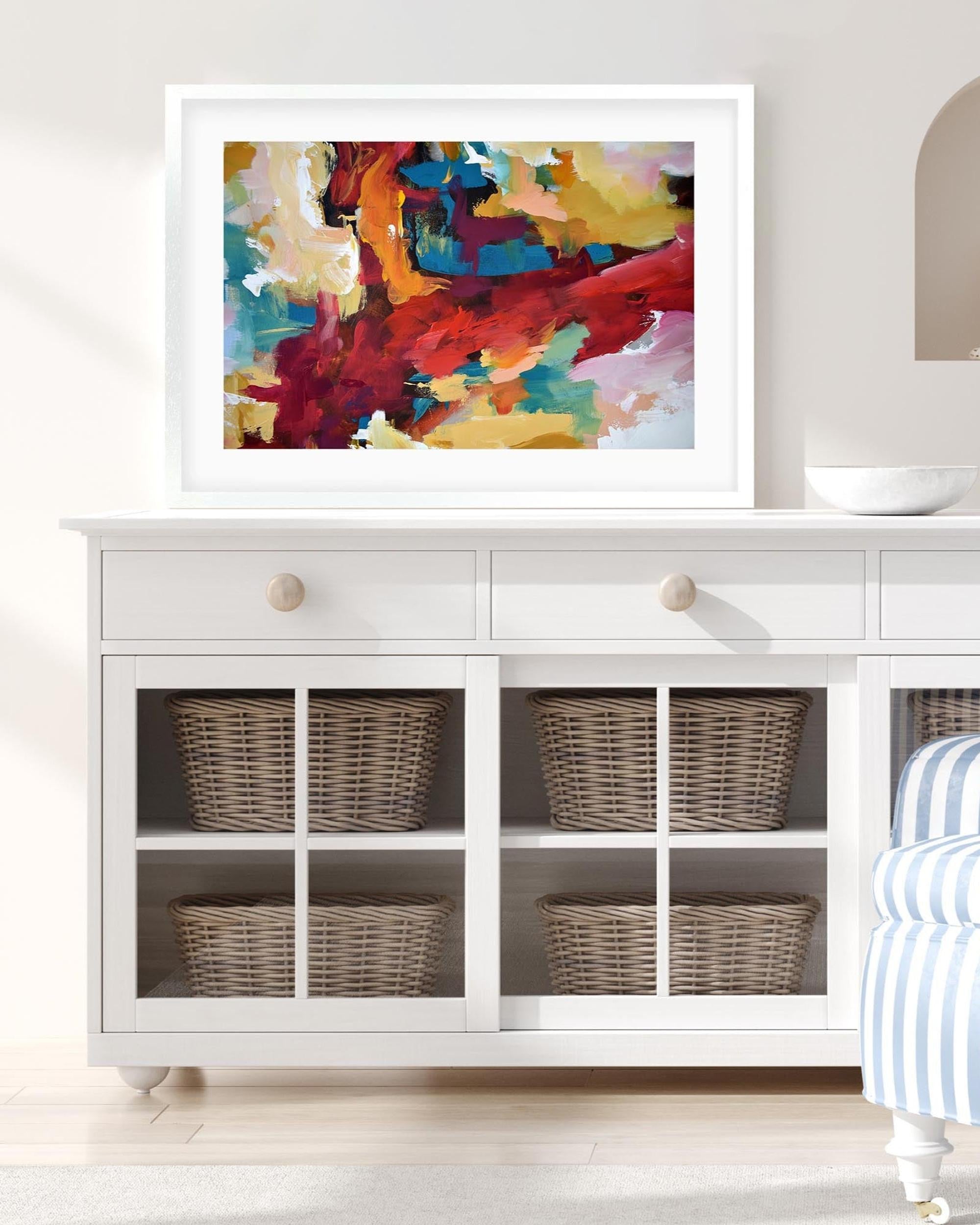 Colorful abstract painting on a white wall above a white cabinet with wicker baskets.