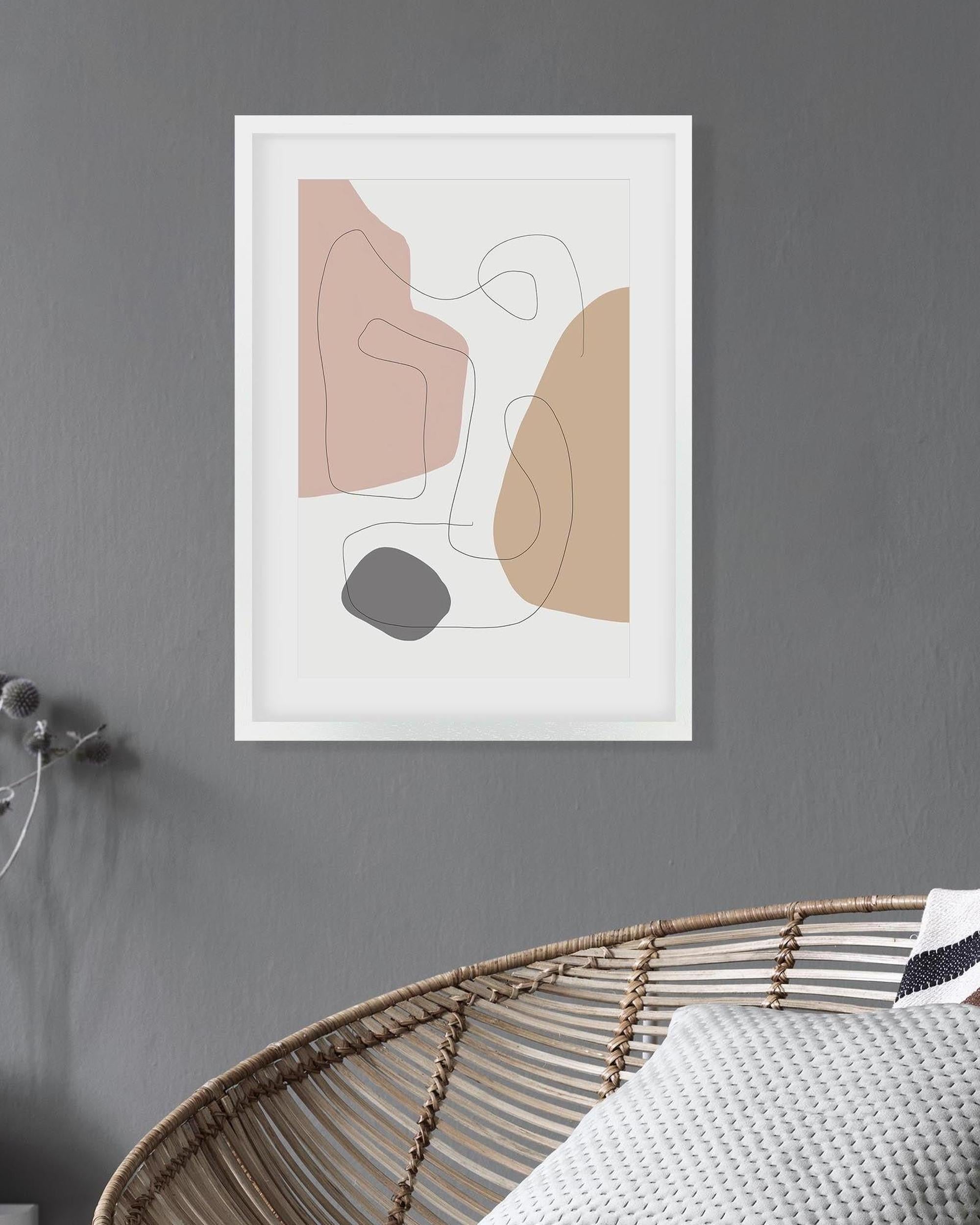 Abstract art print in a white frame on a gray wall with a wicker basket and textured pillows below.