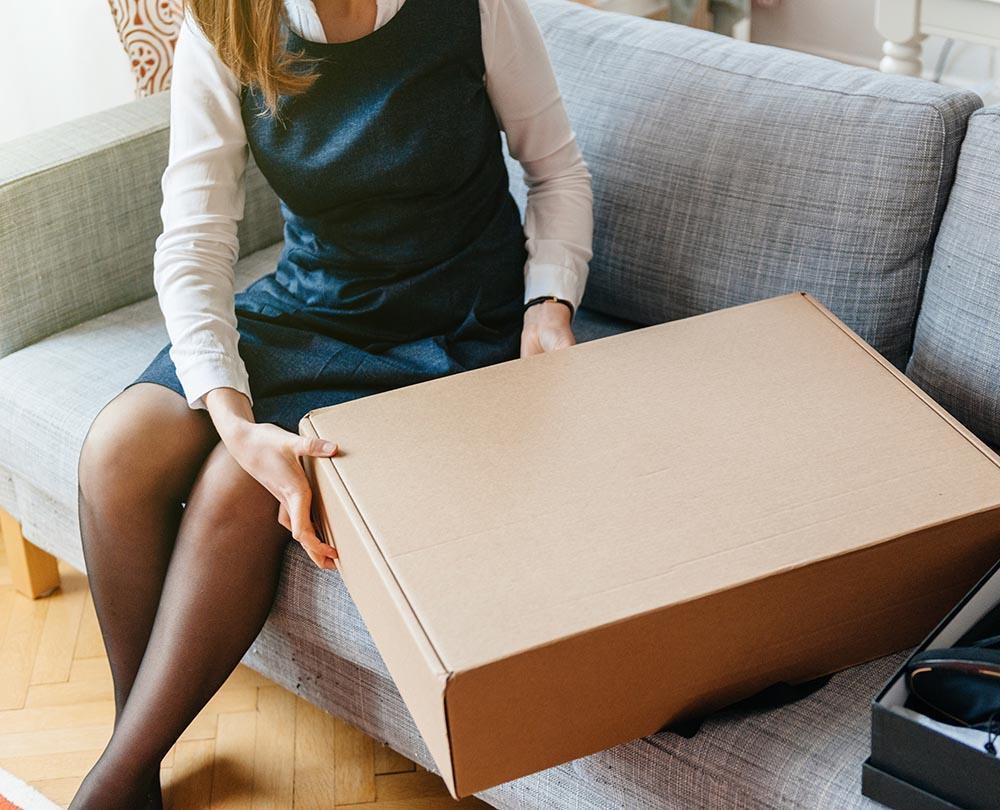 Woman sitting on a couch opening a cardboard box