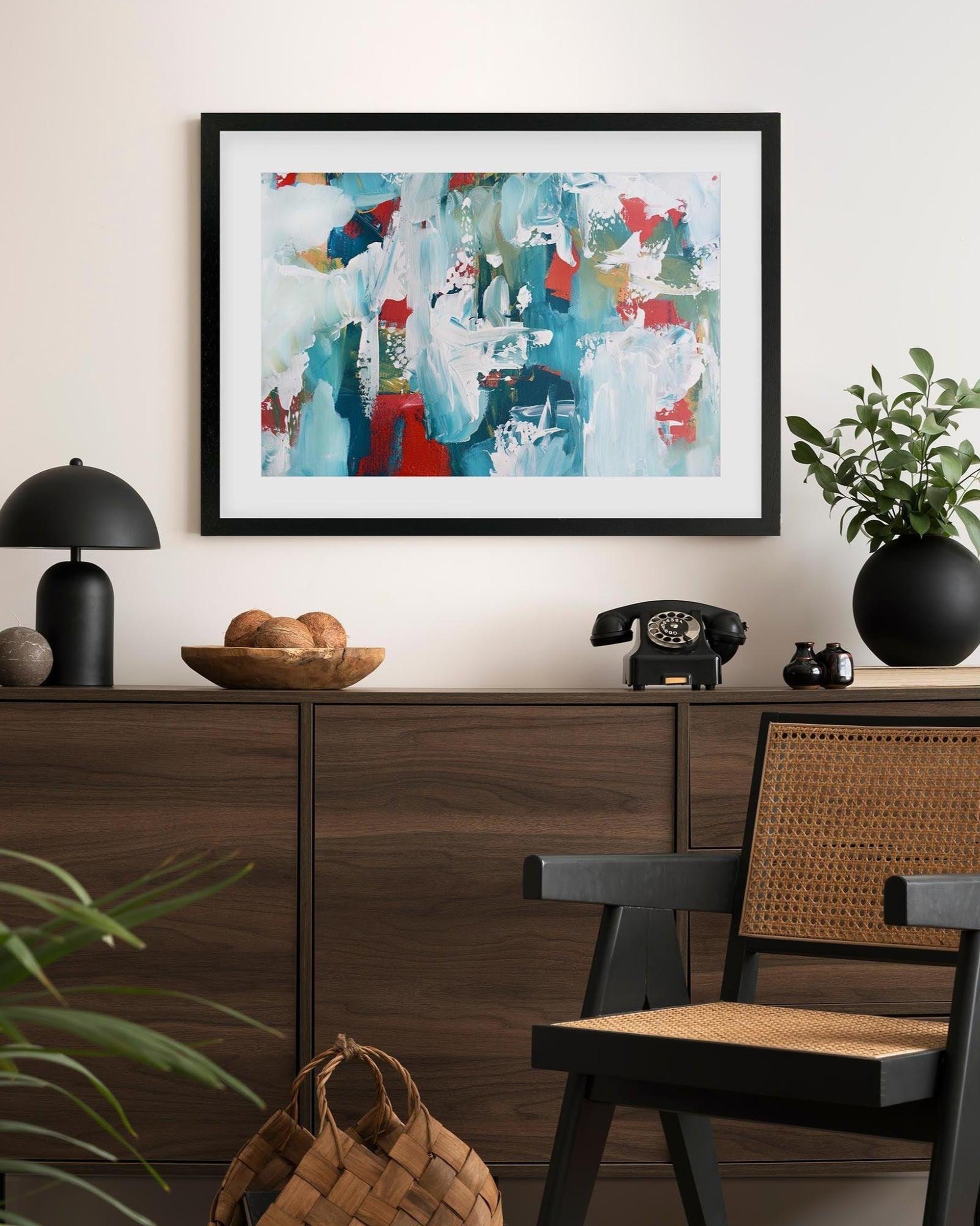 Framed abstract art piece on a wall above a wooden console table with decorative items.