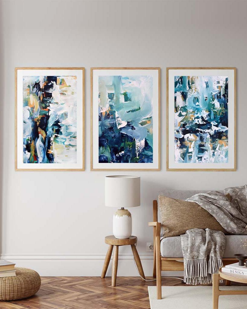 Three abstract paintings in a living room with a sofa and lamp.