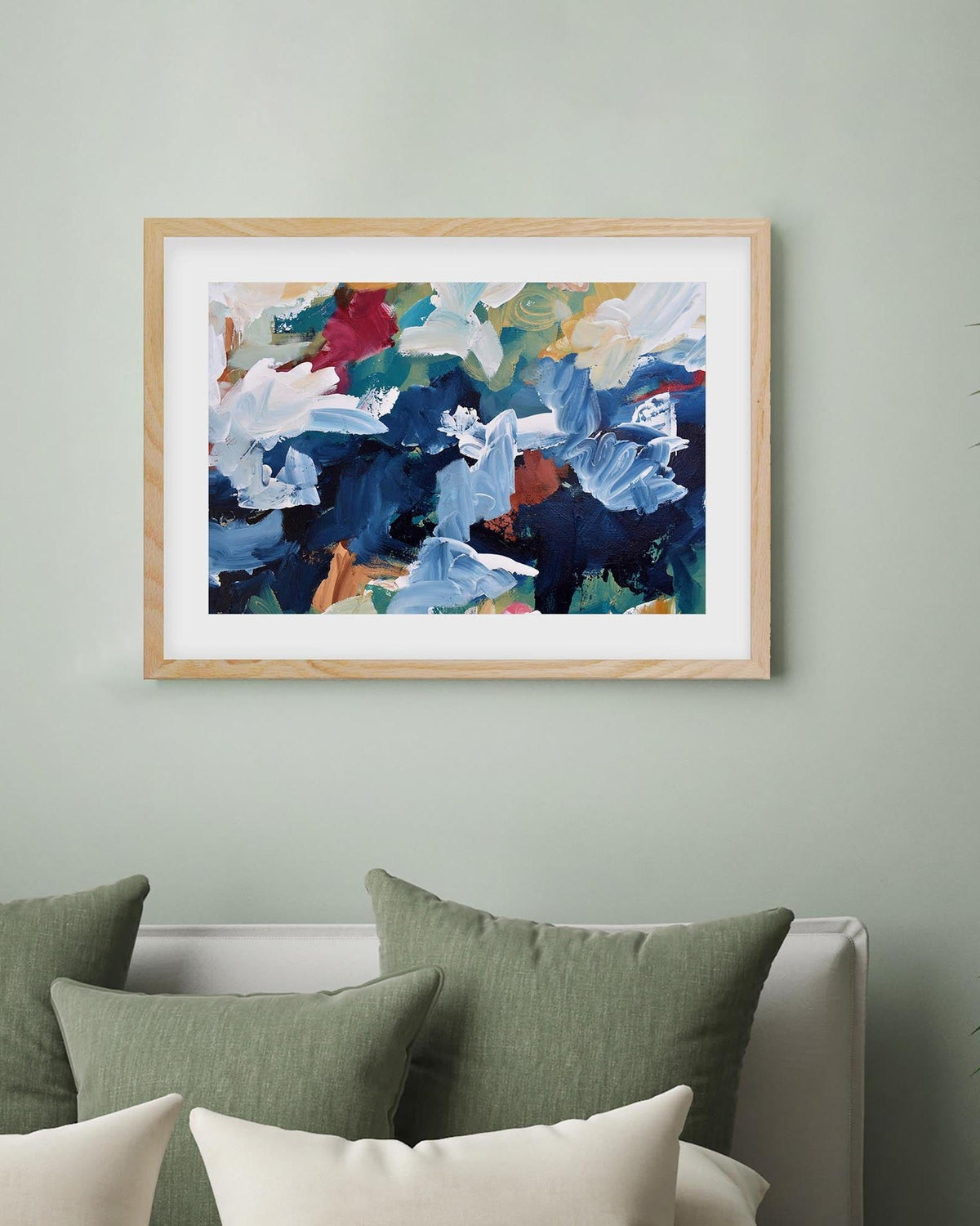 Framed abstract art on a wall with green and white pillows below.