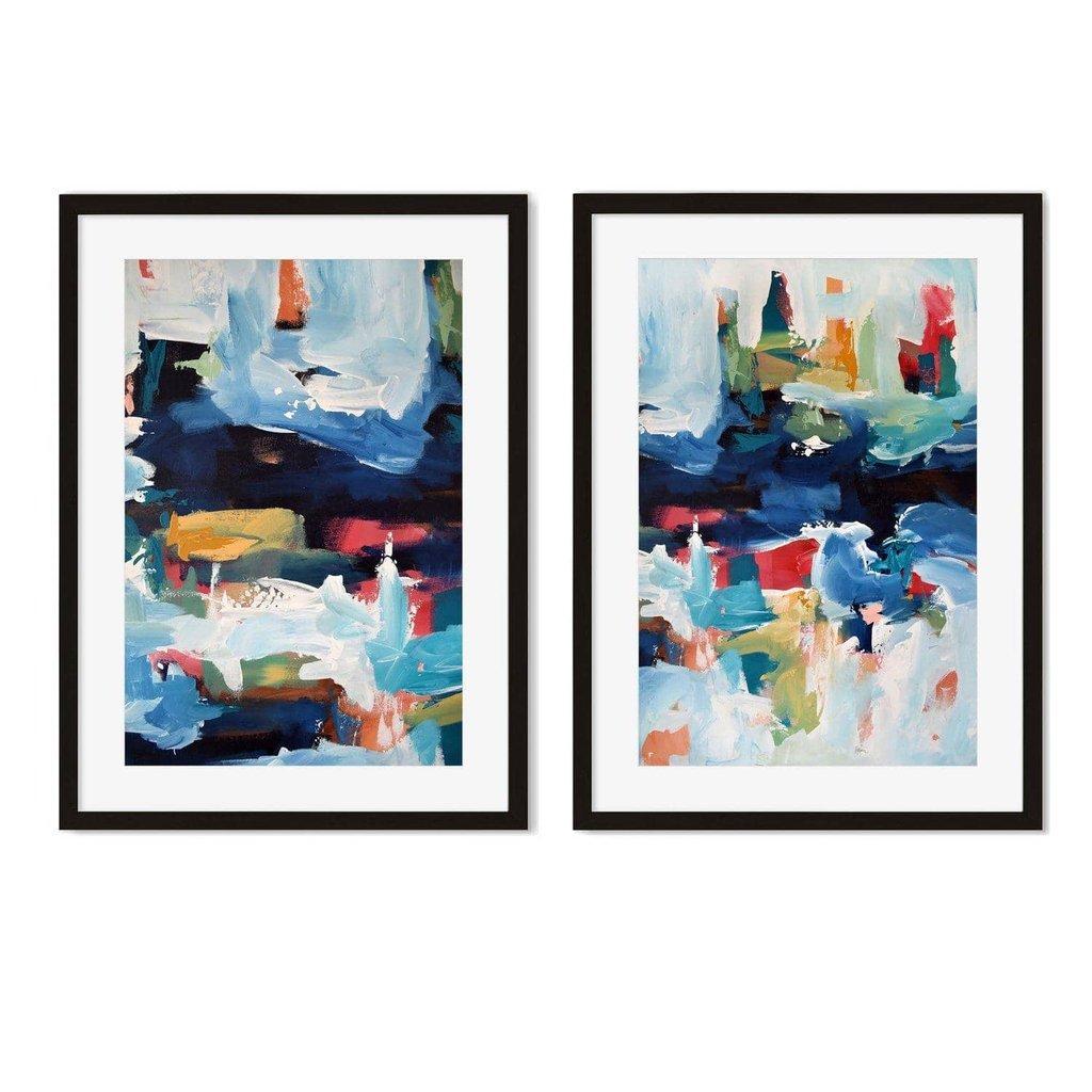 Two framed abstract art prints displayed on a wall above a wooden cabinet, with one print featuring blue tones and the other with a mix of blue and other colors.