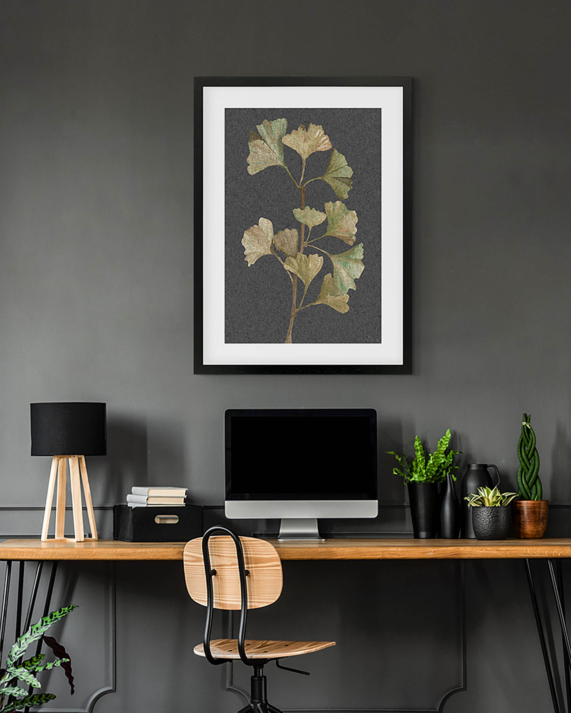 Framed botanical print above a desk with office items on a dark wall.
