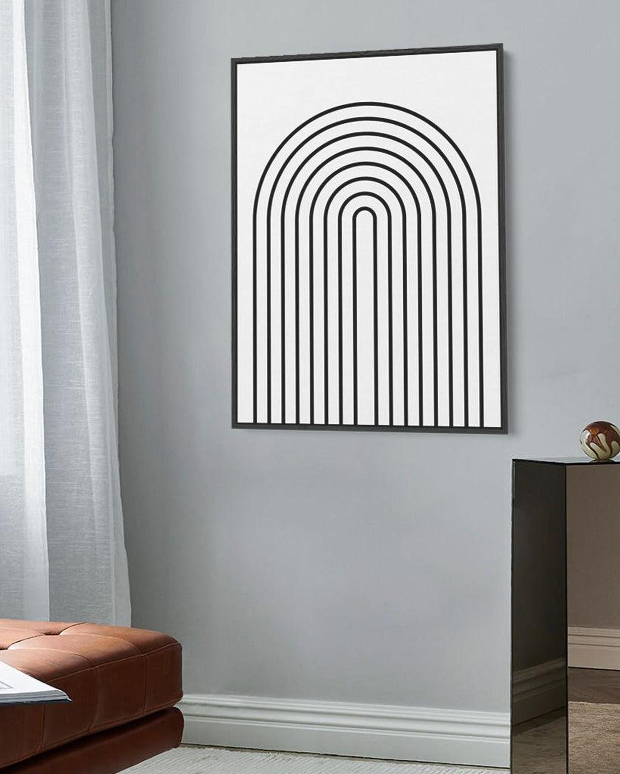 Abstract line art in a black frame on a gray wall with a brown leather sofa.